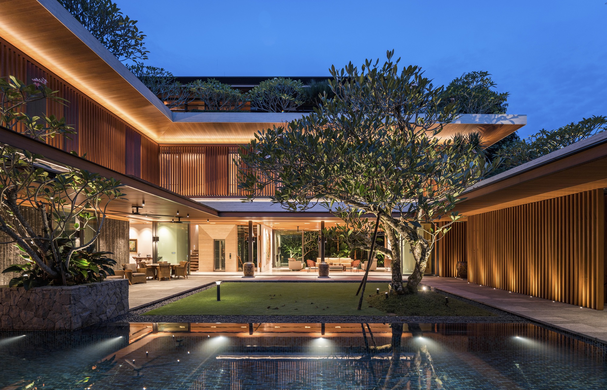 Evening view across the courtyard pool showing two-story timber louvered facades and planted terraces