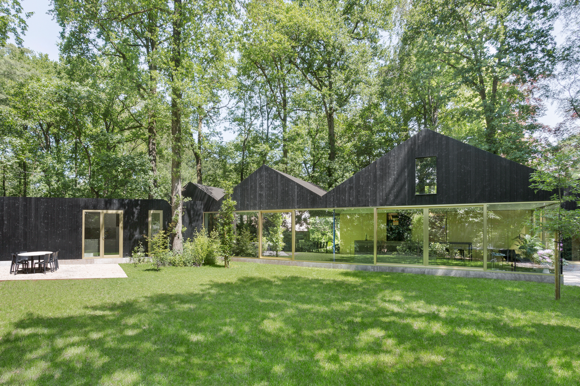 Long view across lawn showing detached dining pavilion and linked volumes beneath mature trees