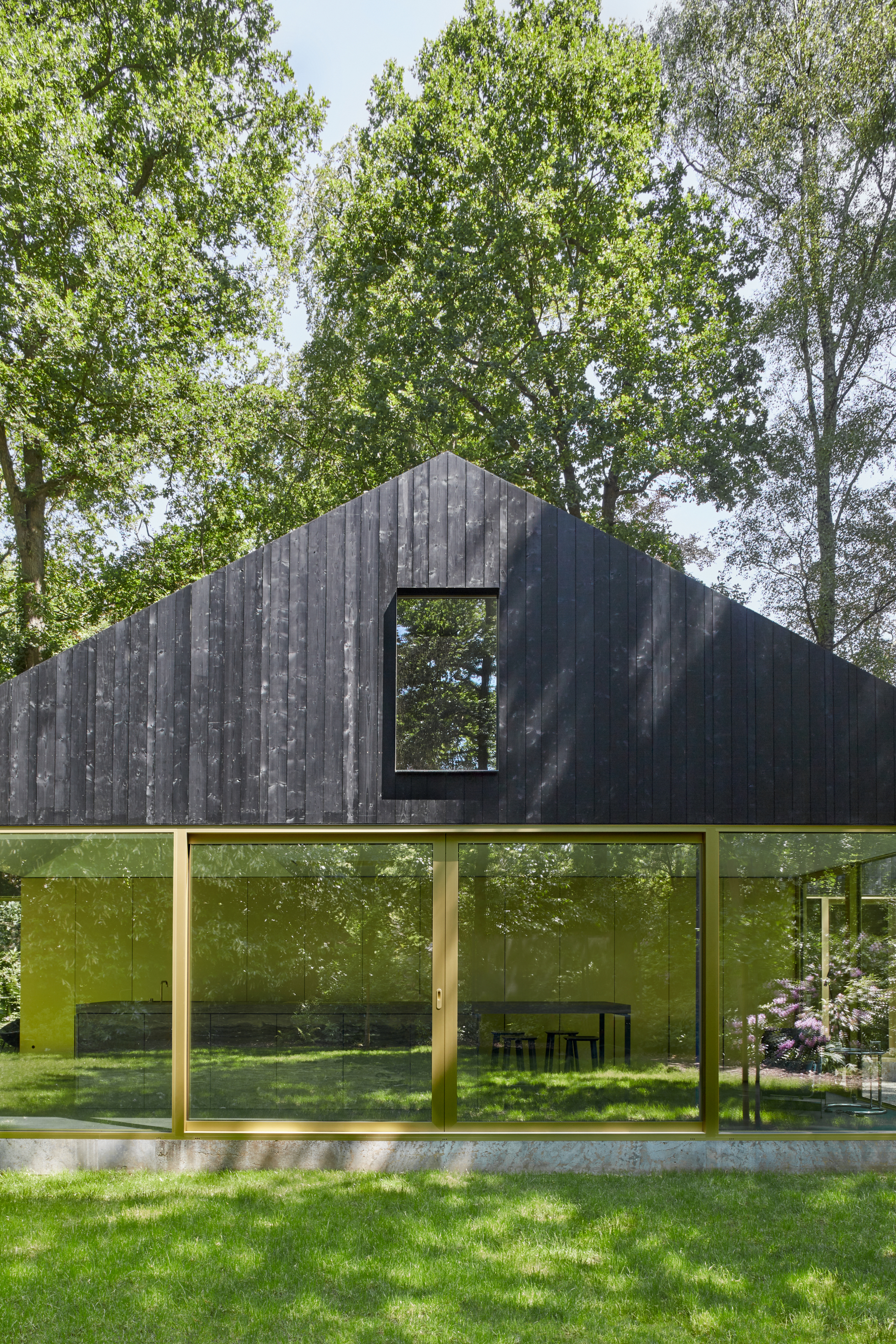 Charred vertical timber facade with a large square window cutout above continuous floor-to-ceiling glazing