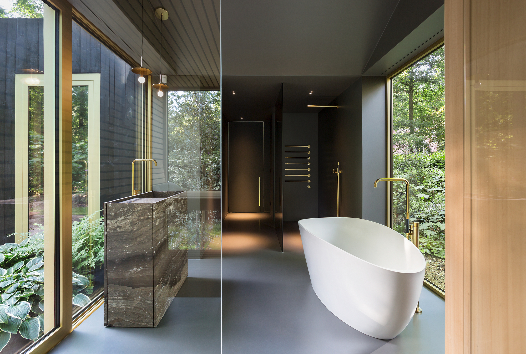 Spa bathroom interior with stone-clad vanity, freestanding tub, and floor-to-ceiling windows facing lush greenery