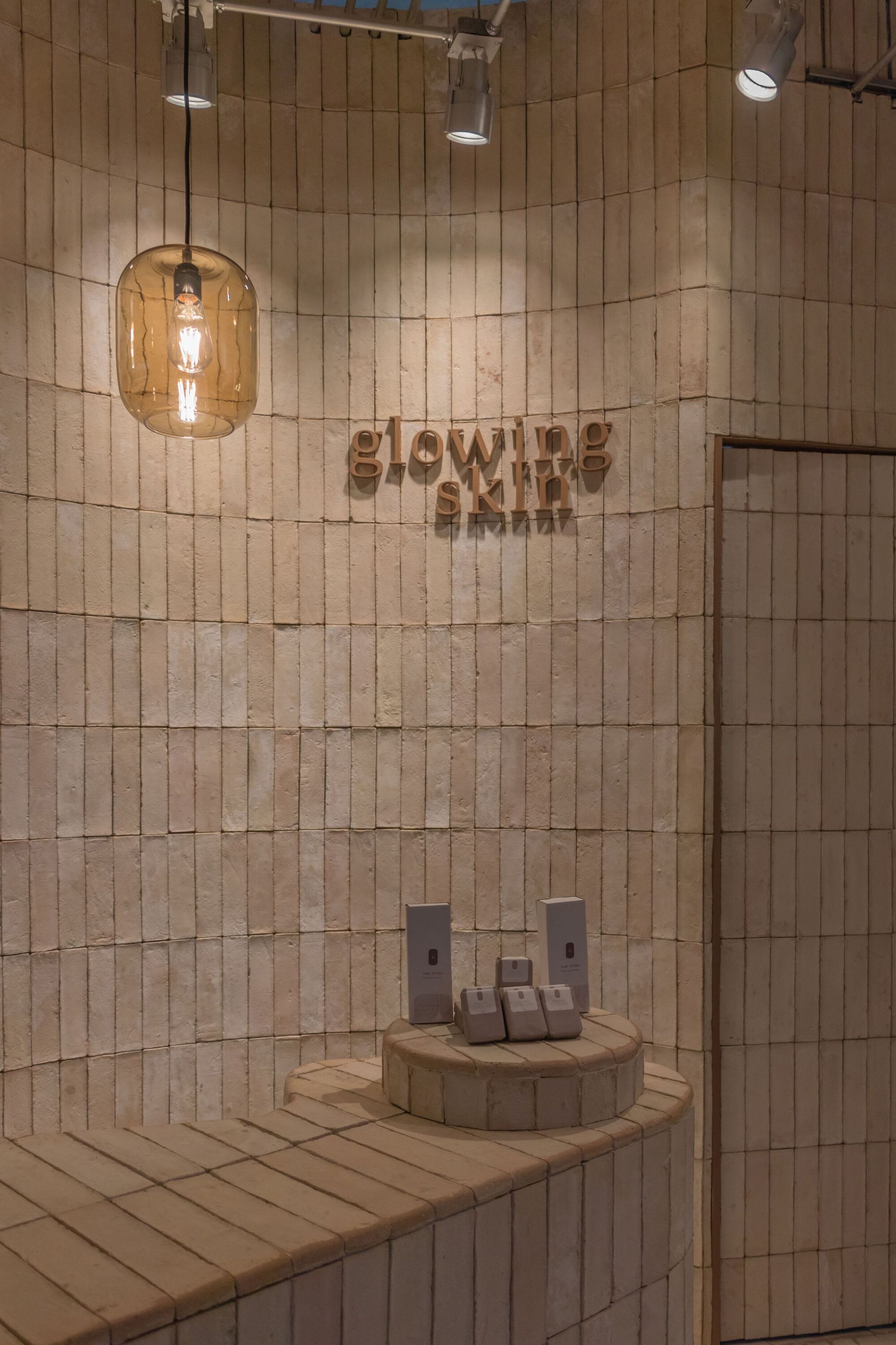 Curved wood-tiled wall with branded signage and amber glass pendant light overhead