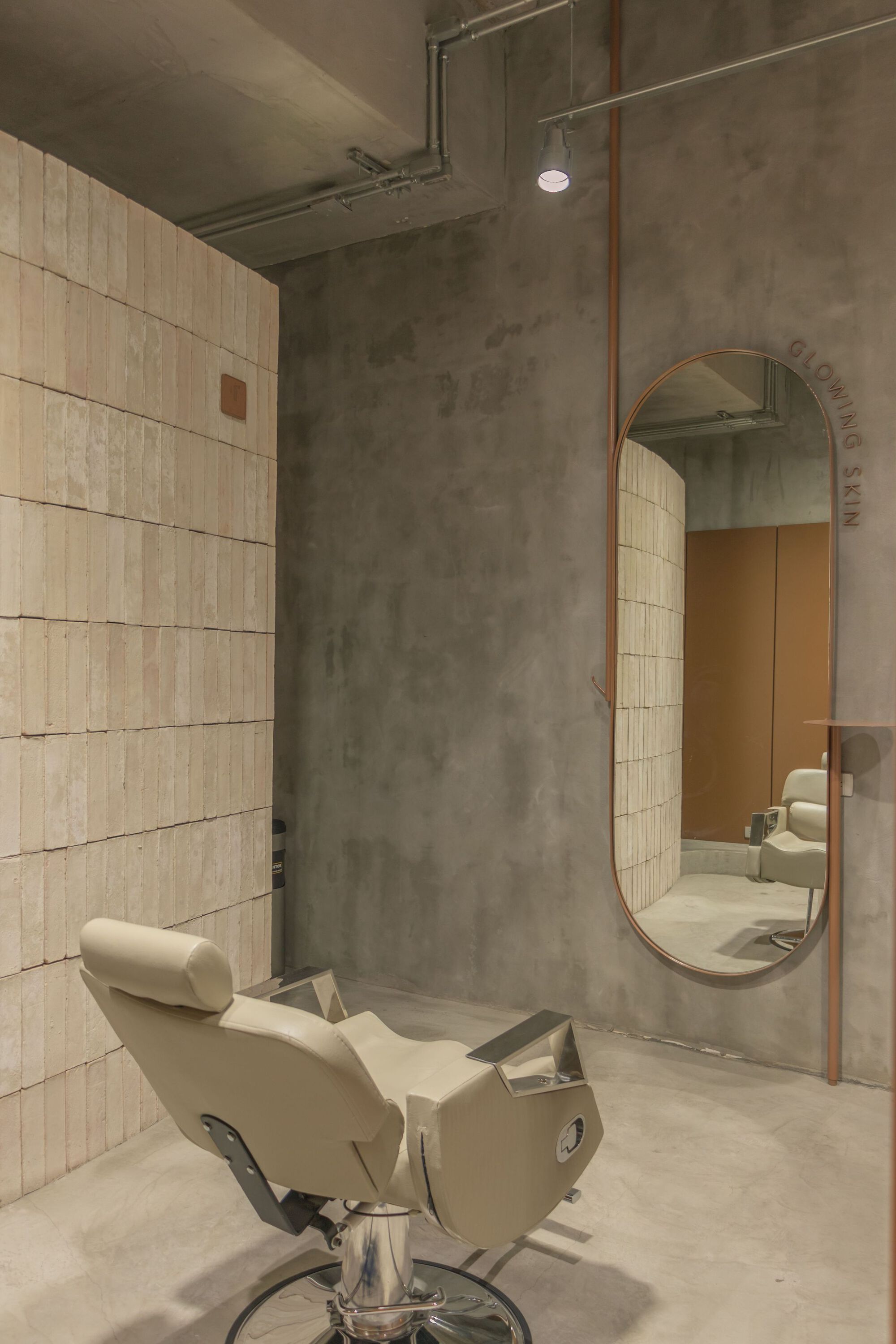 Salon chair beneath oval mirror framed in copper against polished concrete wall