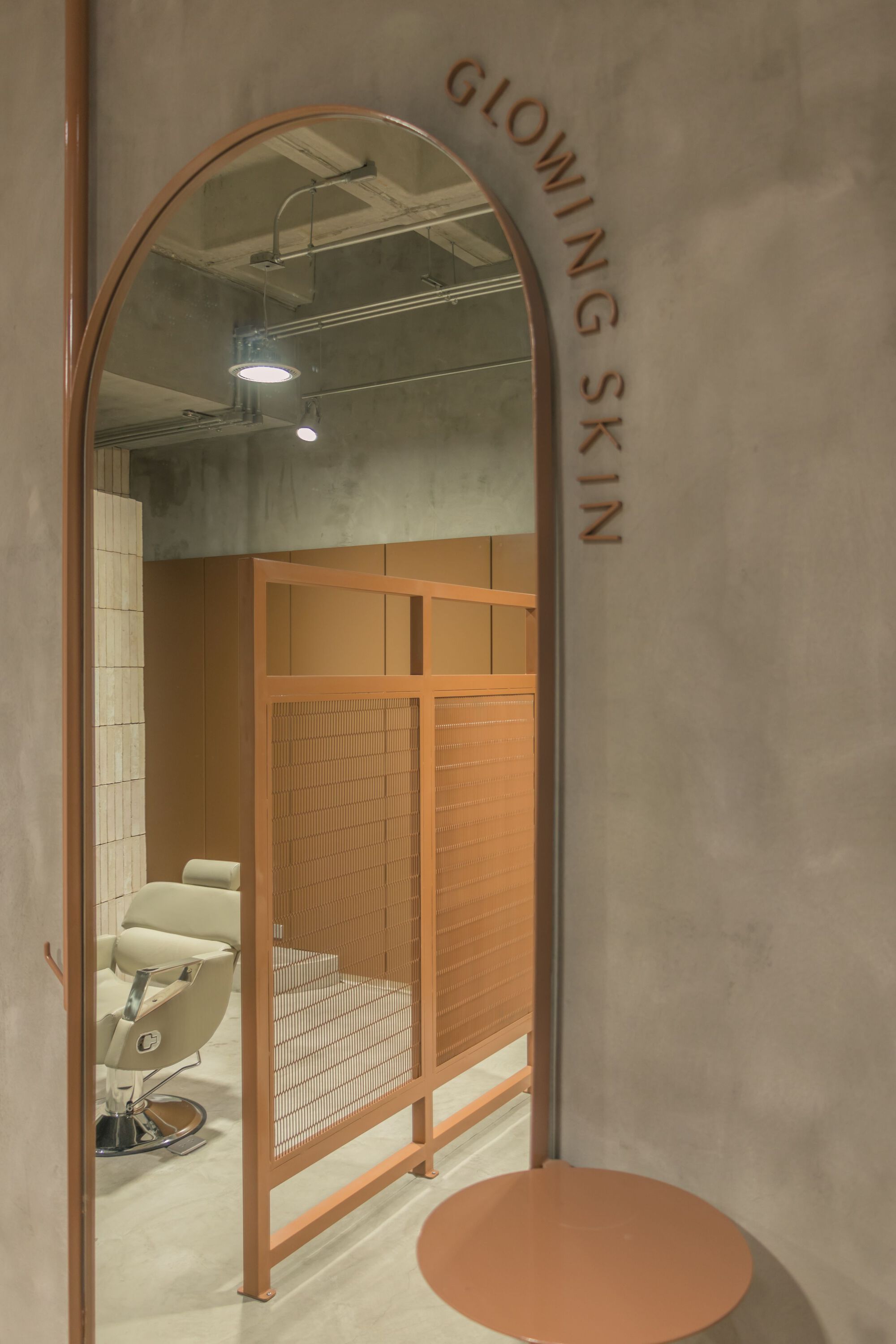 Copper arched mirror reflecting salon station through doorway with lettering on grey plaster wall