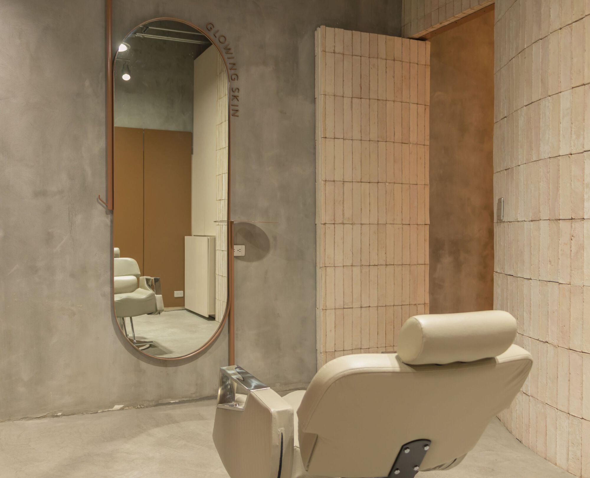 Reclined salon chair with oval mirror and vertical tile wall under exposed ceiling conduits