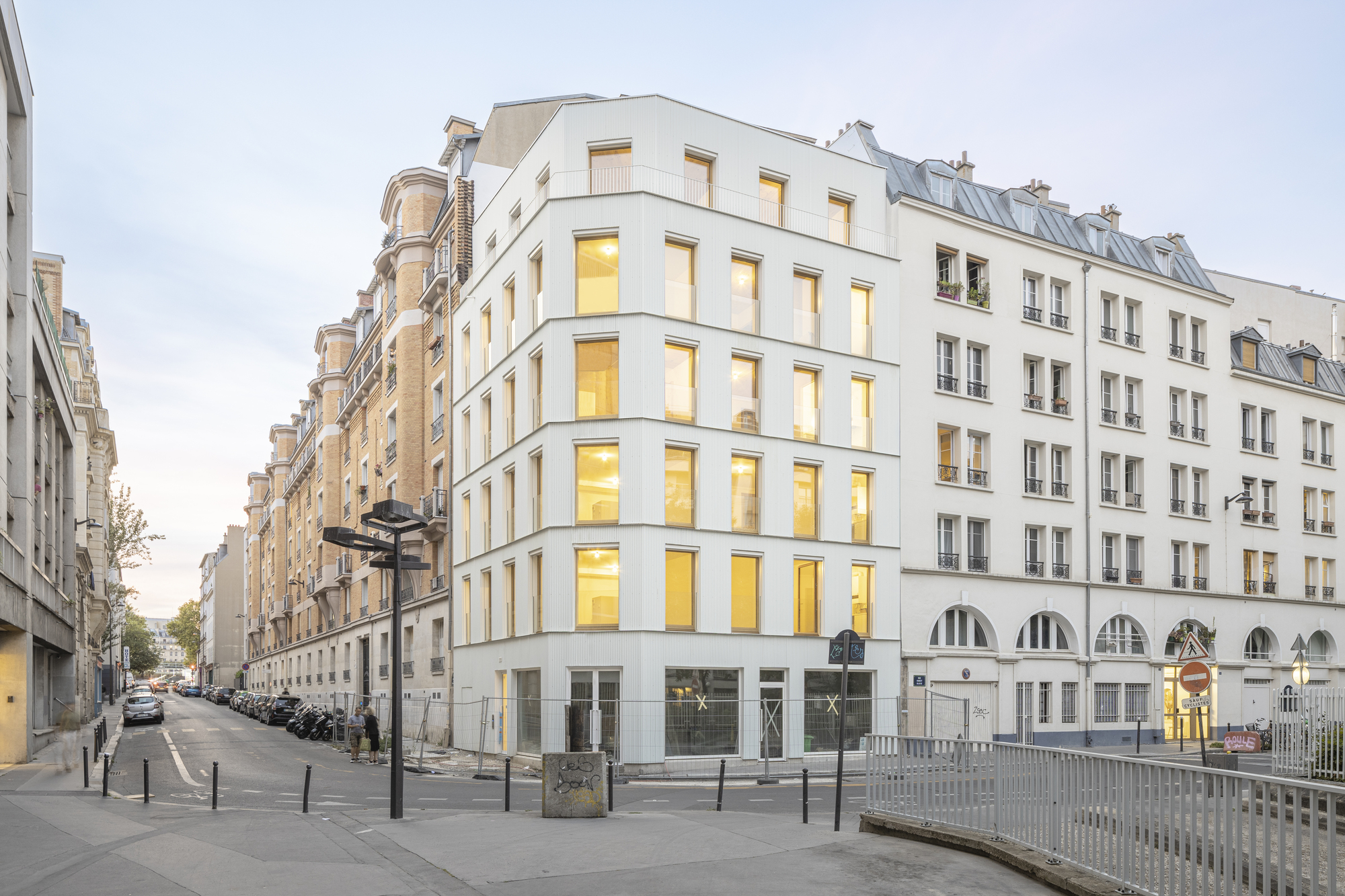 Corner view of the white facade with inset windows and arched ground floor openings at dusk