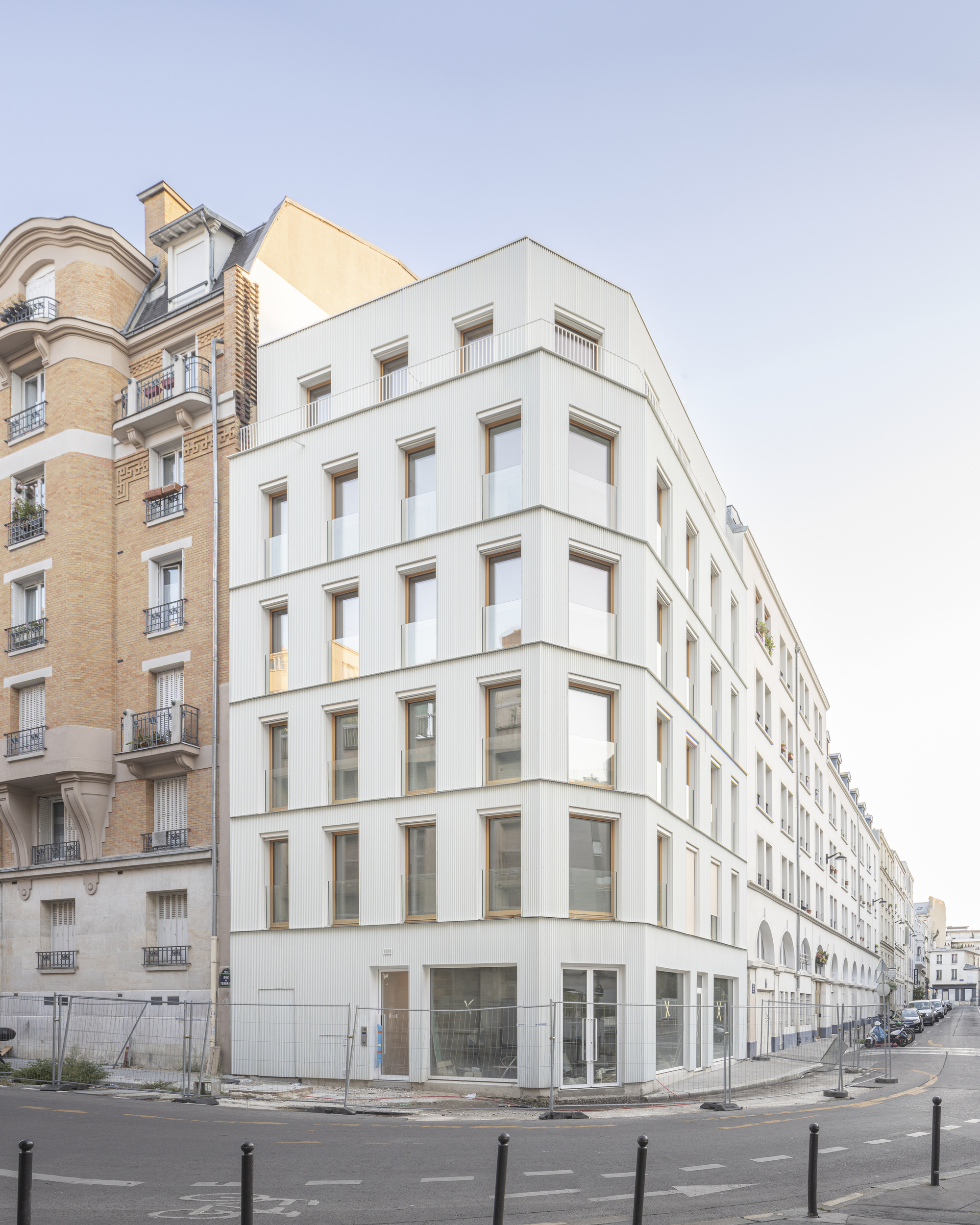 White facade with recessed timber-framed windows wrapping around the street corner at daylight