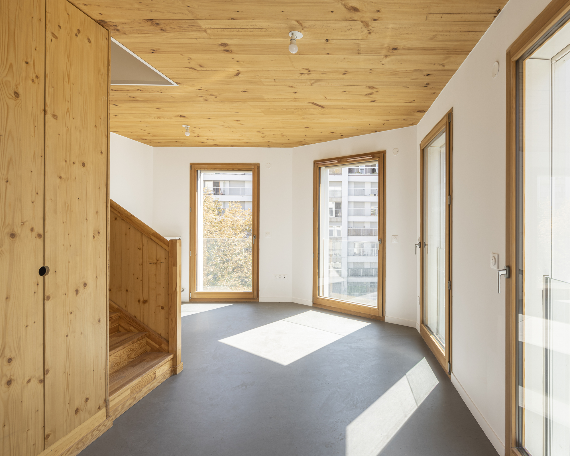 Interior room with timber-paneled ceiling, grey flooring and two windows casting sunlight across the space