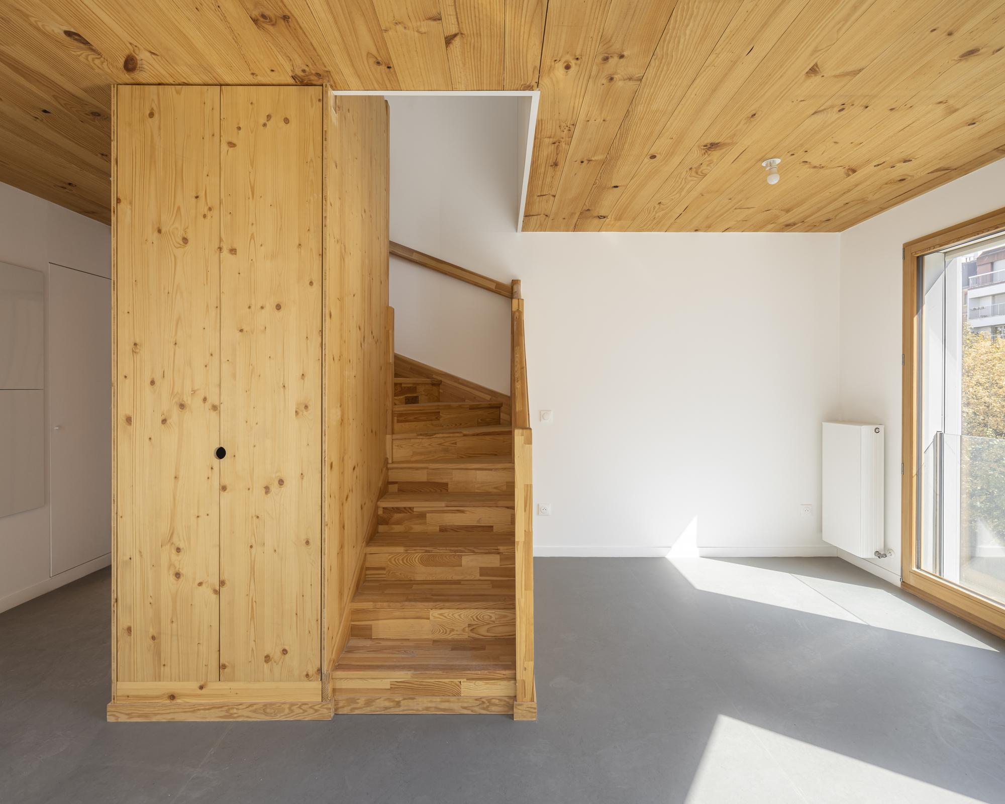 Timber staircase wrapped with wooden wall panels beside a grey floor and pine ceiling