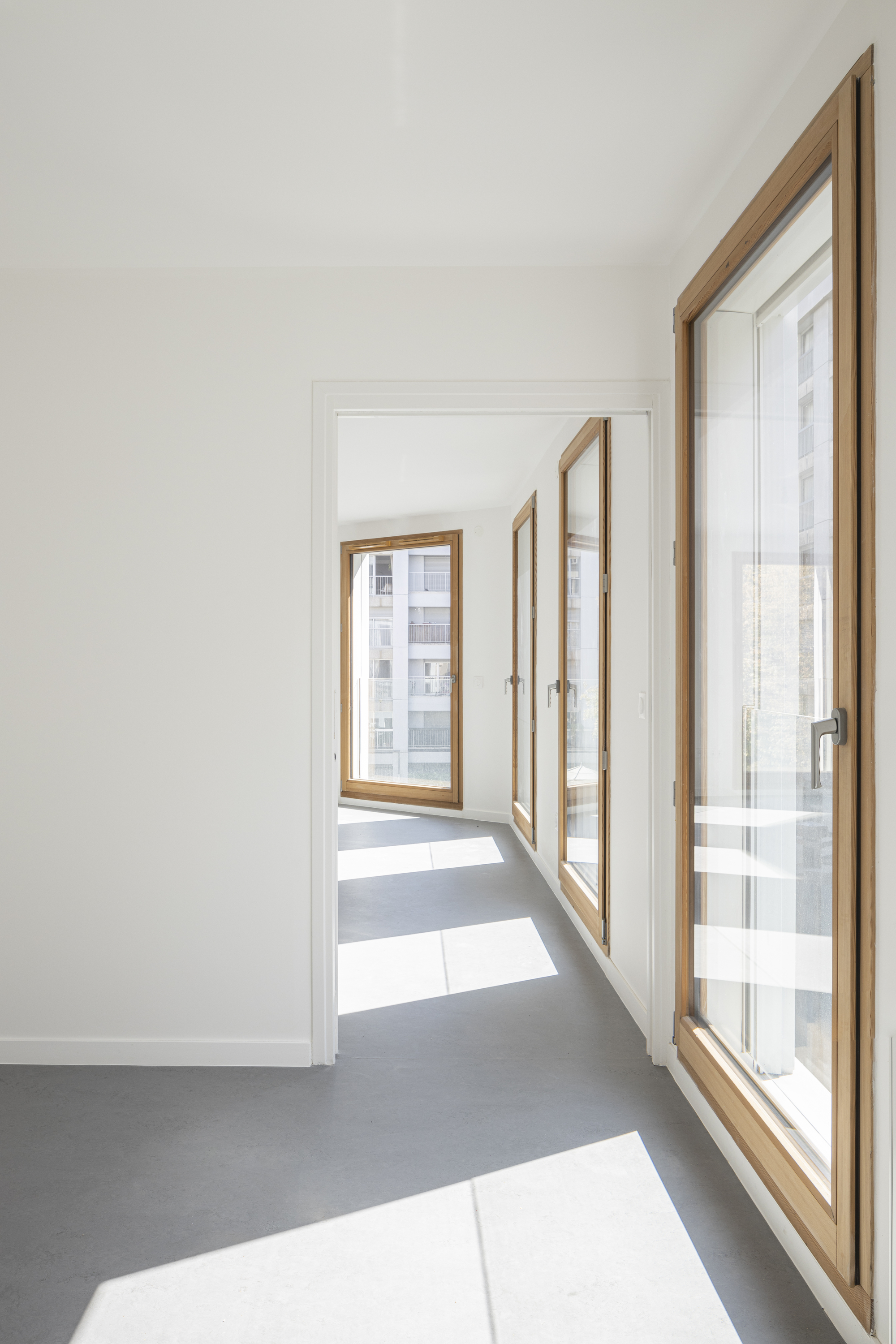 Corridor with timber-framed casement windows creating angled patches of sunlight on the grey floor