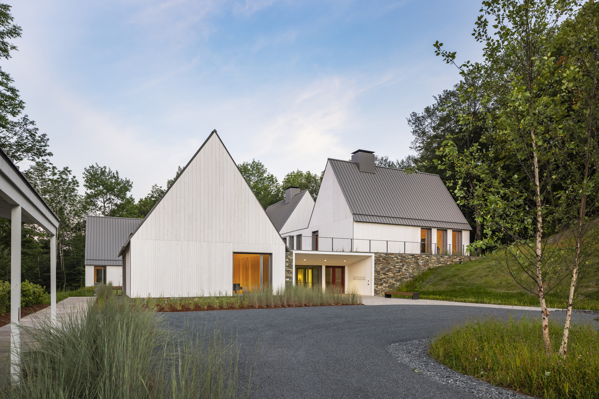 Entry courtyard view of white vertical-board gabled buildings with stone base walls at dusk