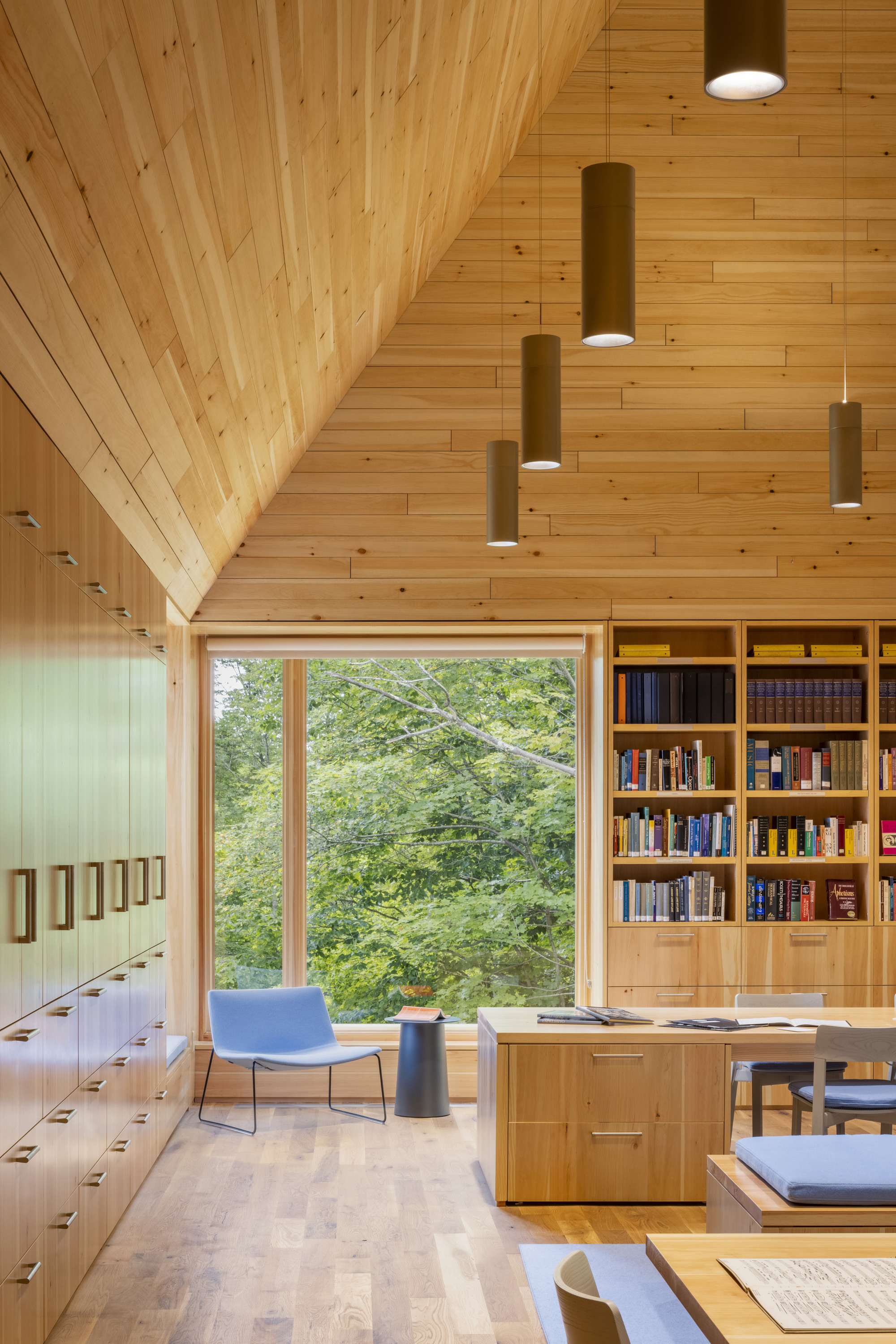 Library corner with built-in bookshelves, reading table, and large window facing the forested hillside