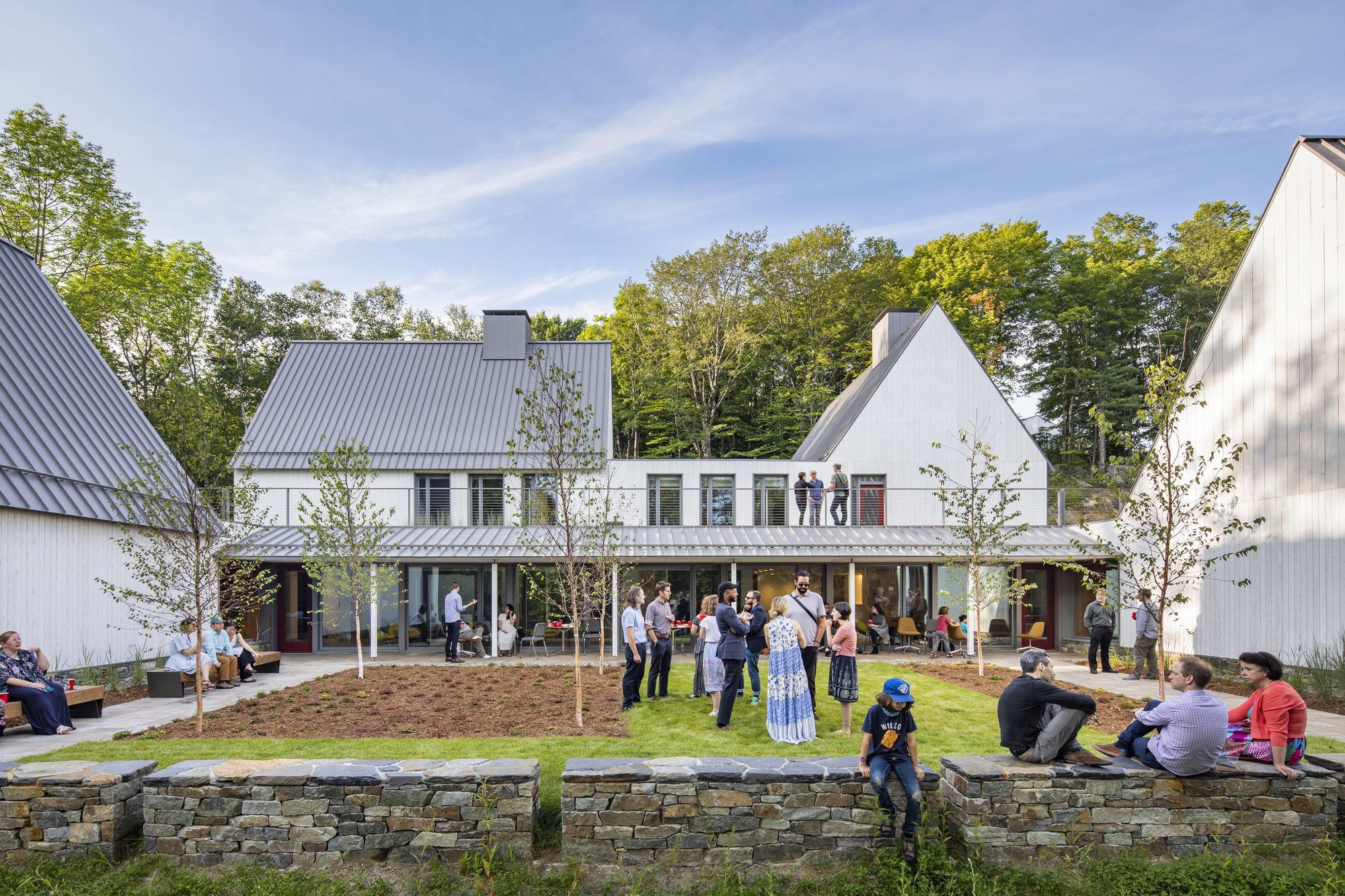 White gabled buildings around a lawn with visitors gathering on an afternoon under blue sky