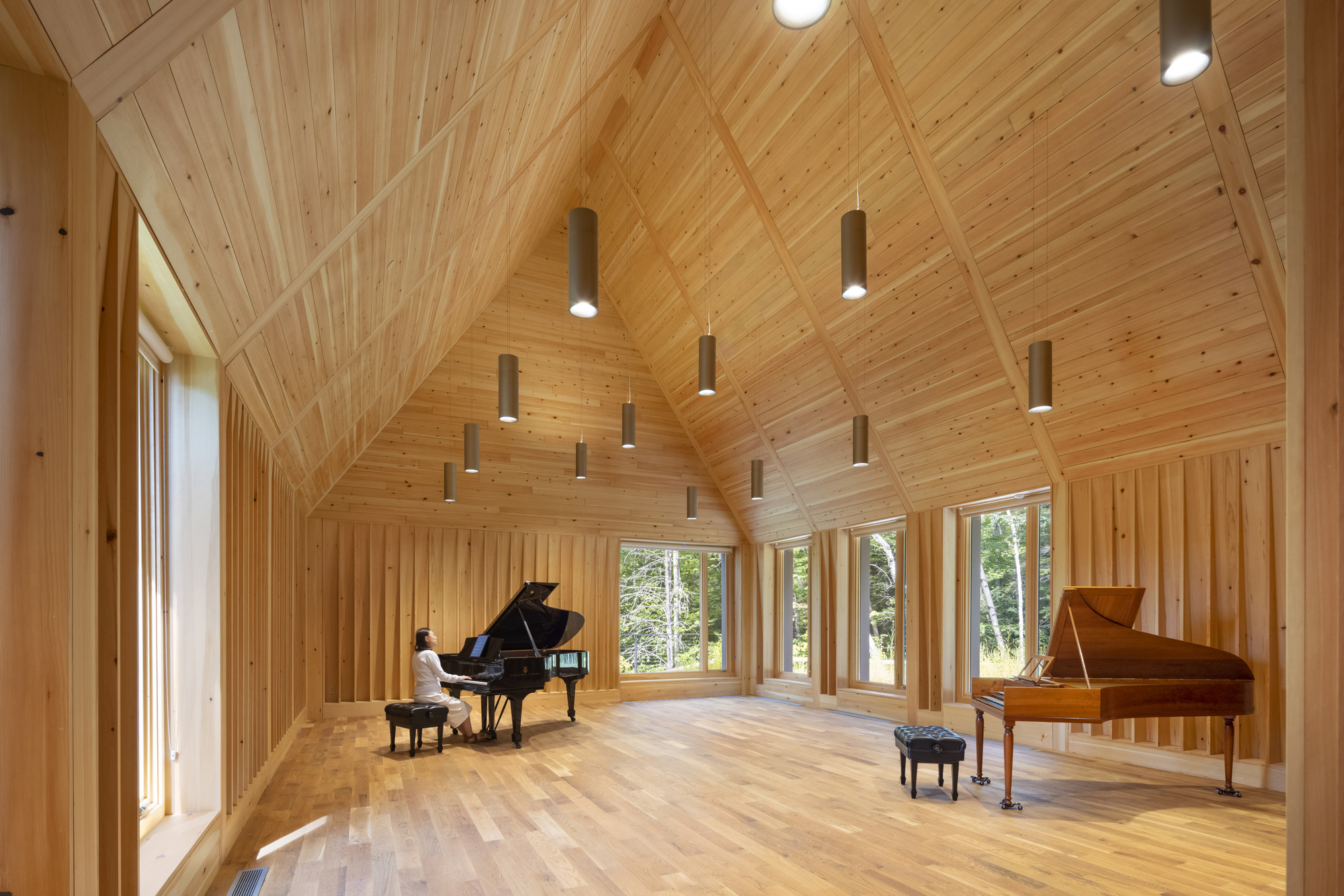 Interior of a timber-lined rehearsal hall with vaulted ceiling and pendant lights above two grand pianos