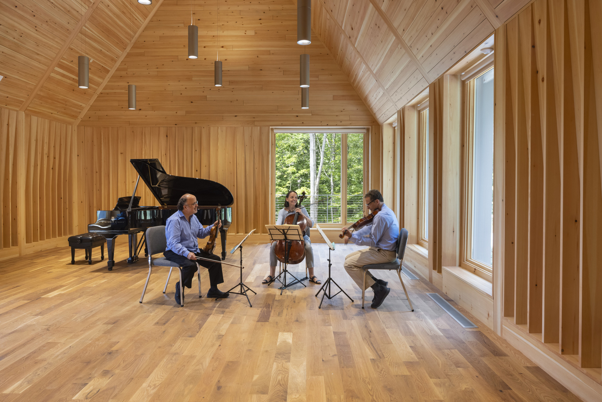 Musicians performing in the timber-paneled room with tall windows overlooking trees