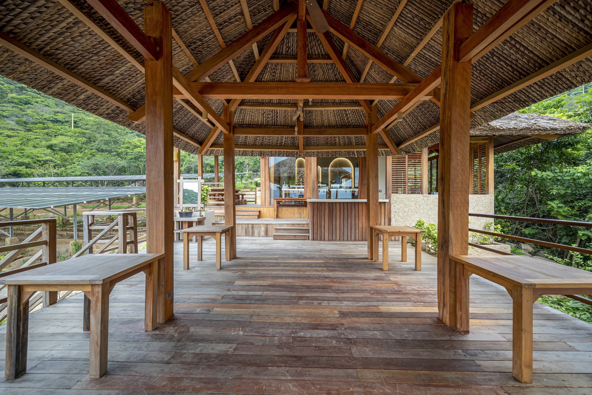 Open timber pavilion with thatched roof, exposed rafters and wooden benches on a raised deck