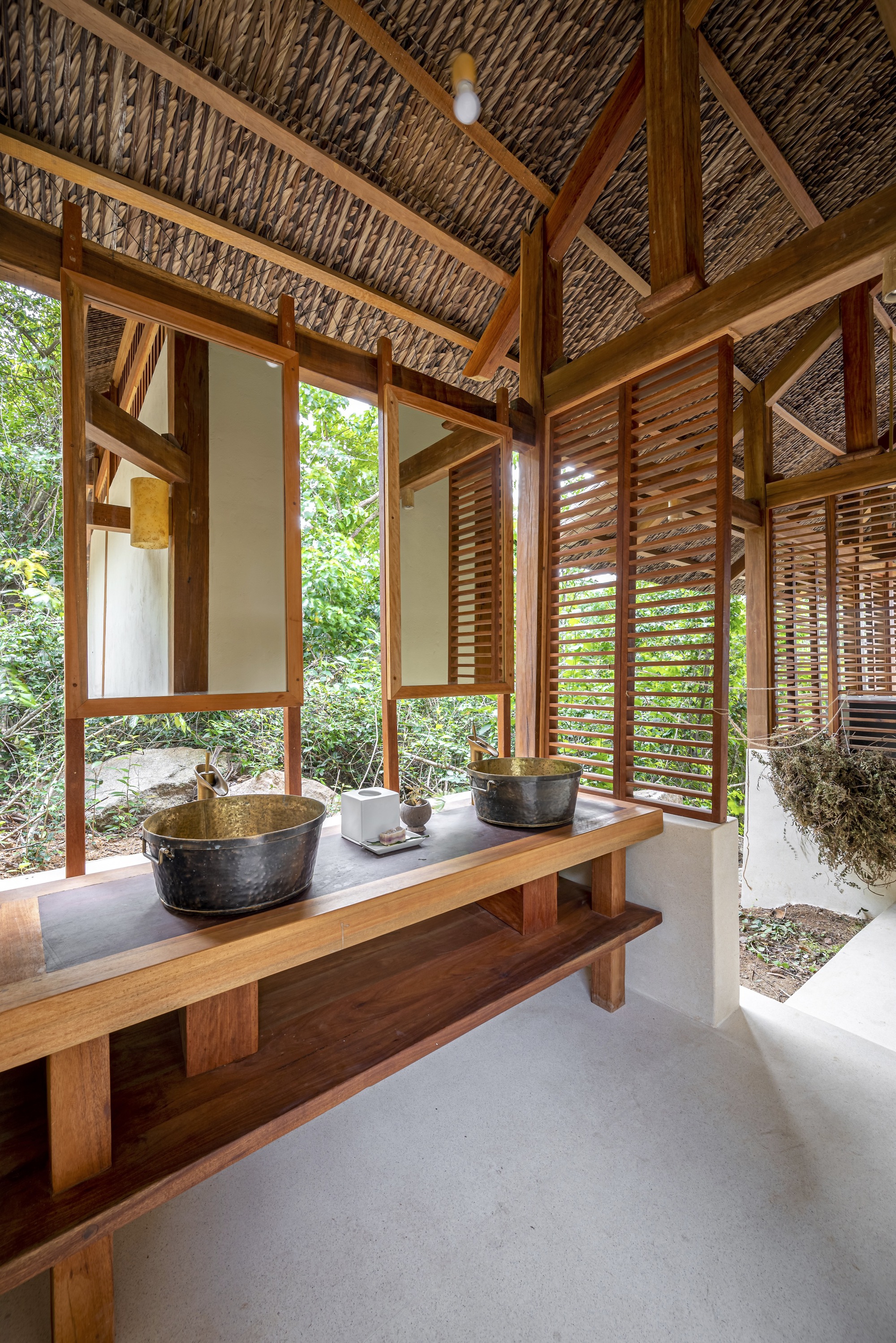 Bathroom with timber vanity, stone vessel sinks and louvered screens opening to garden vegetation