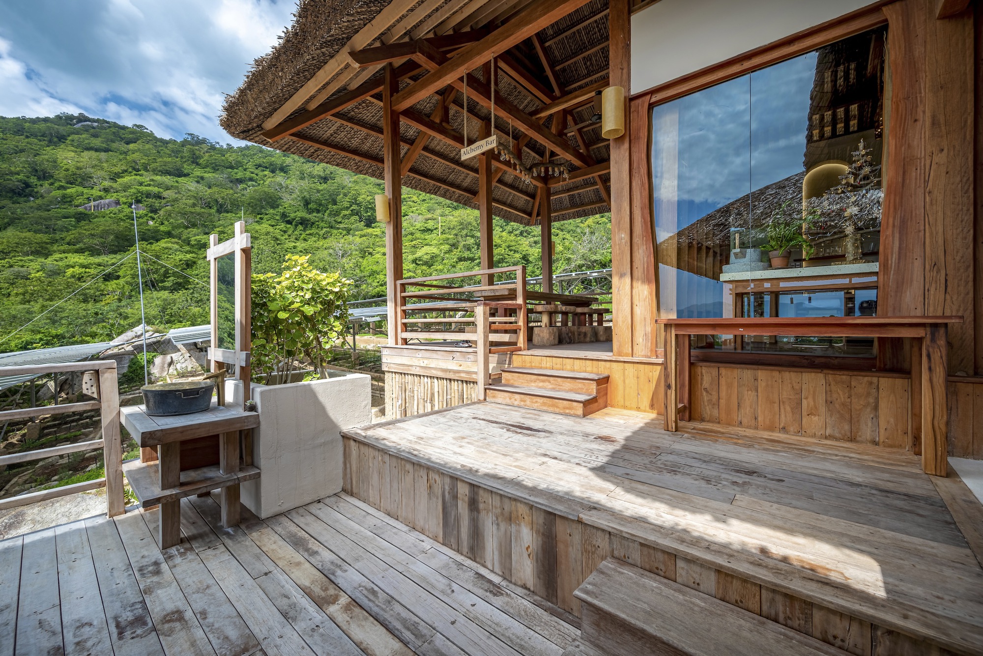 Corner deck platform with timber bench seating under thatched eaves and mountain view