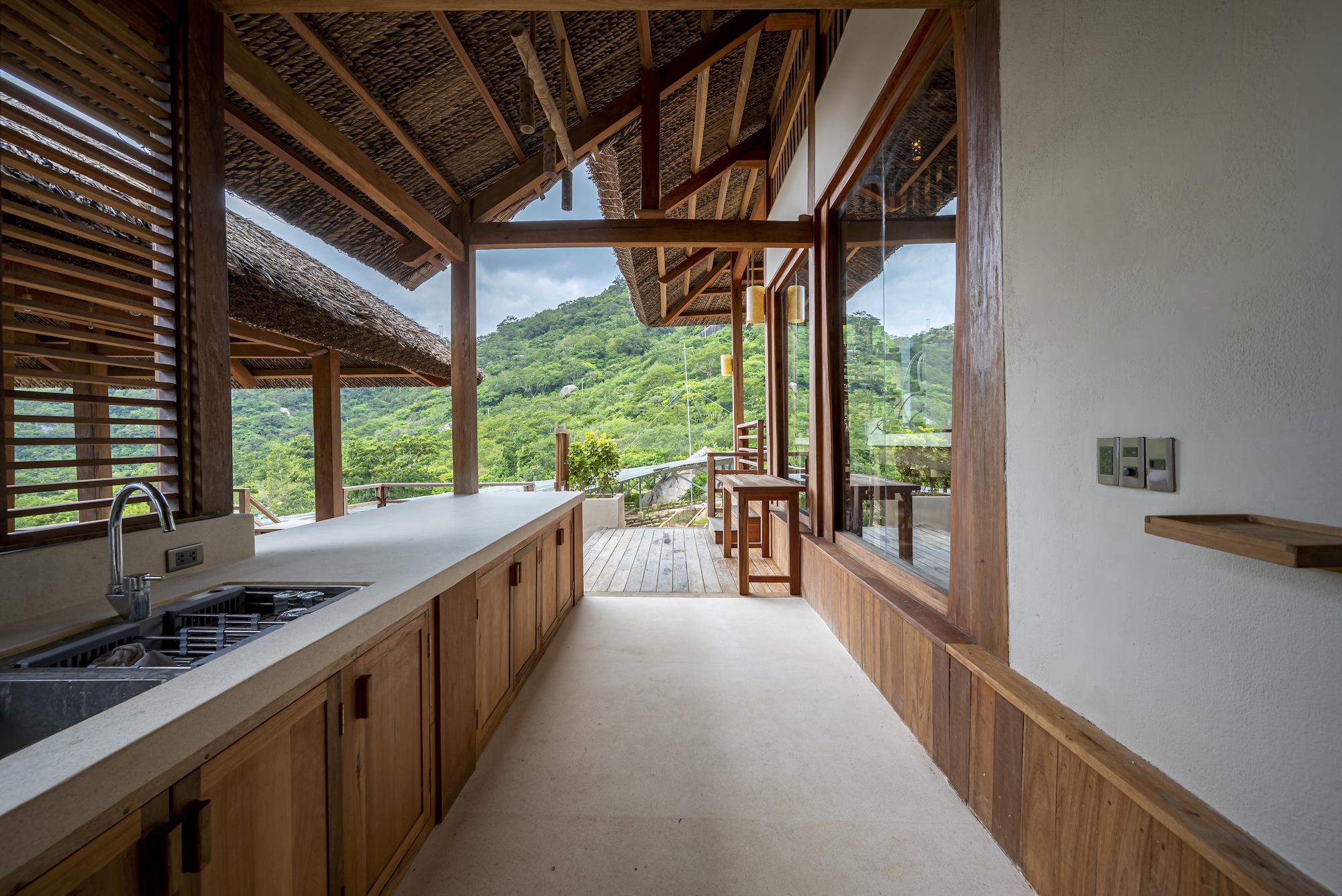 Kitchen counter with timber cabinetry and concrete floor opening to covered deck with valley view