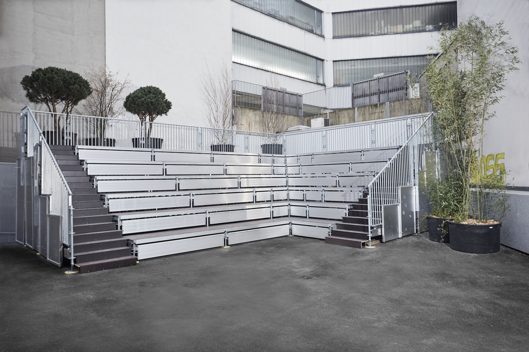 Metal bleacher seating with planted trees in containers on an outdoor courtyard terrace