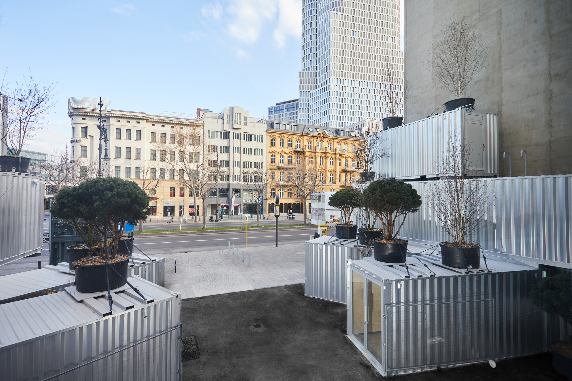 Courtyard view of corrugated metal container modules with planted trees facing the surrounding urban blocks