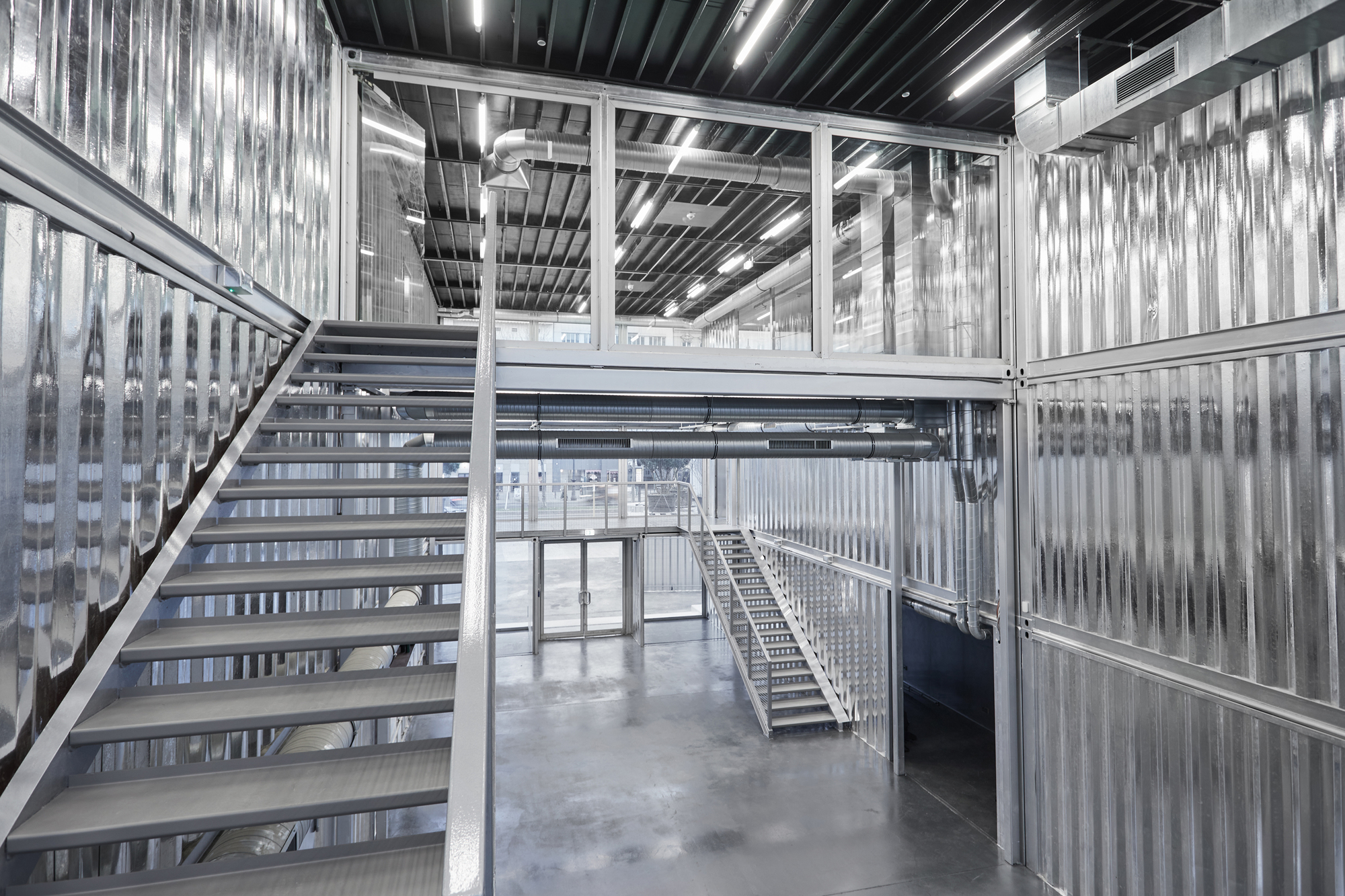 Steel staircase ascending between translucent corrugated walls beneath black ceiling with linear lighting strips