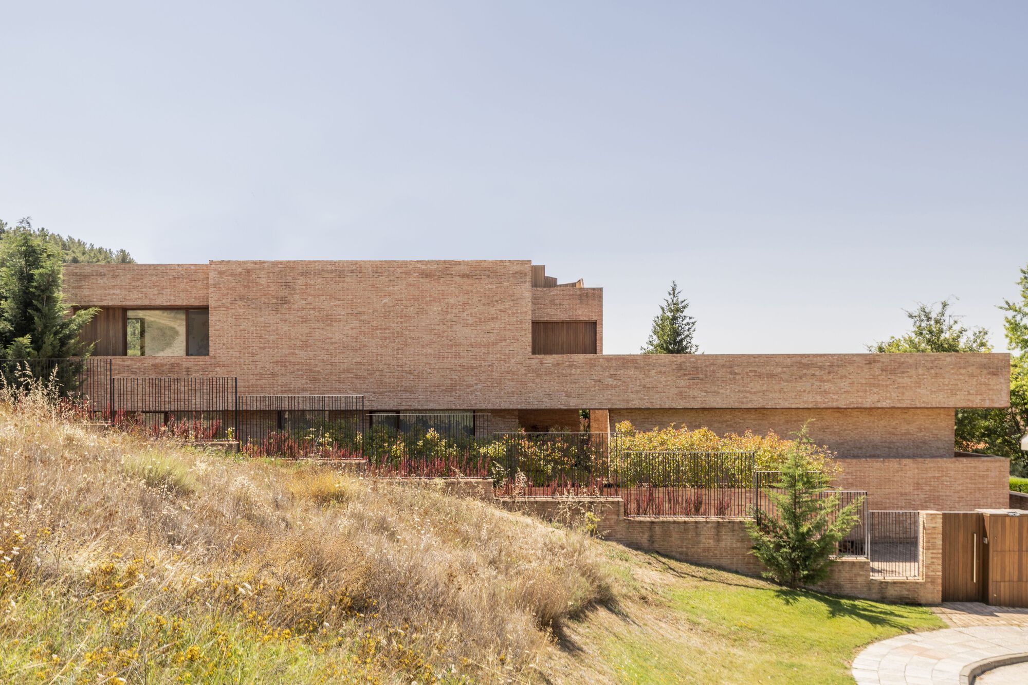 Stepped brick facade with planted terraces descending a sloped site with dry grasses