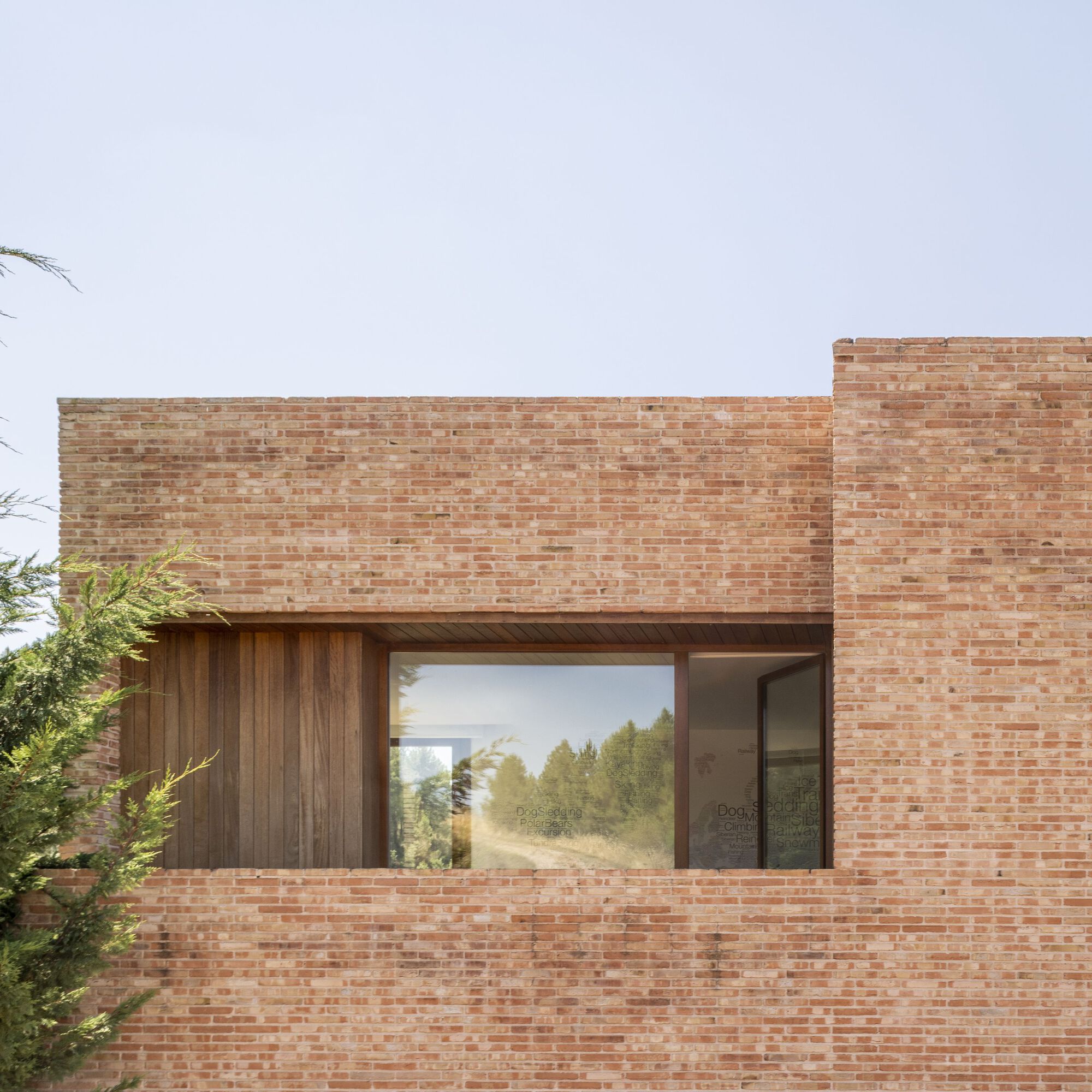 Horizontal window set into a brick facade with timber cladding beneath an overcast sky