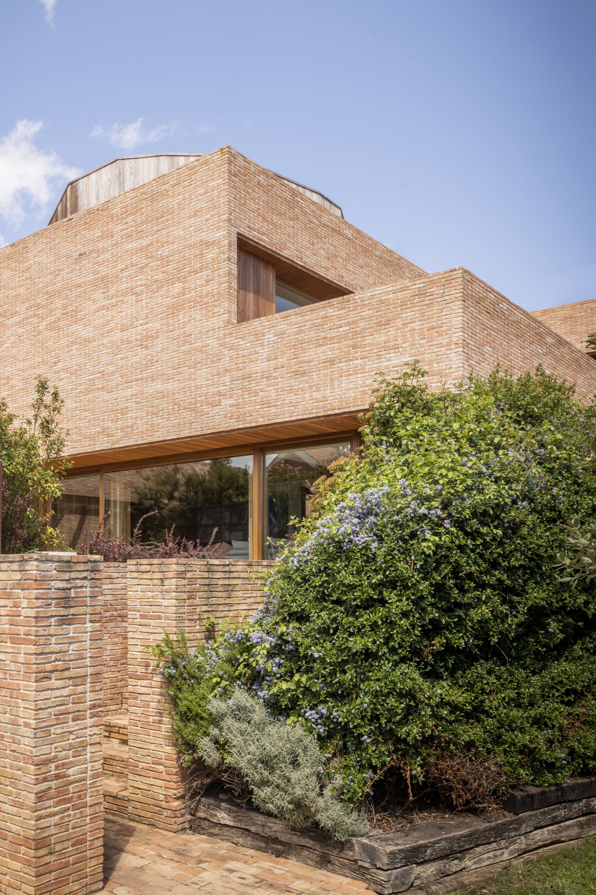 Cantilevered brick facade above a glazed living space with planted beds below