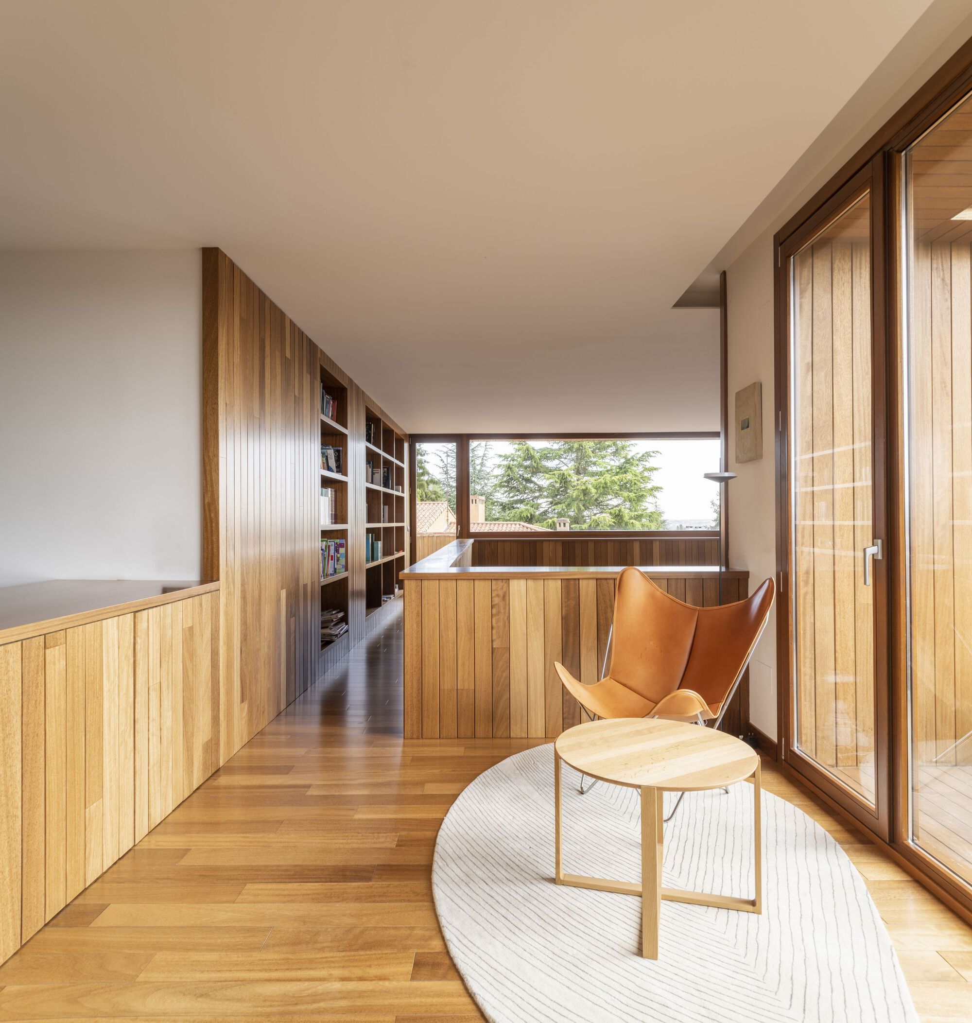 Hallway seating area with timber slat walls and bookshelf overlooking a courtyard