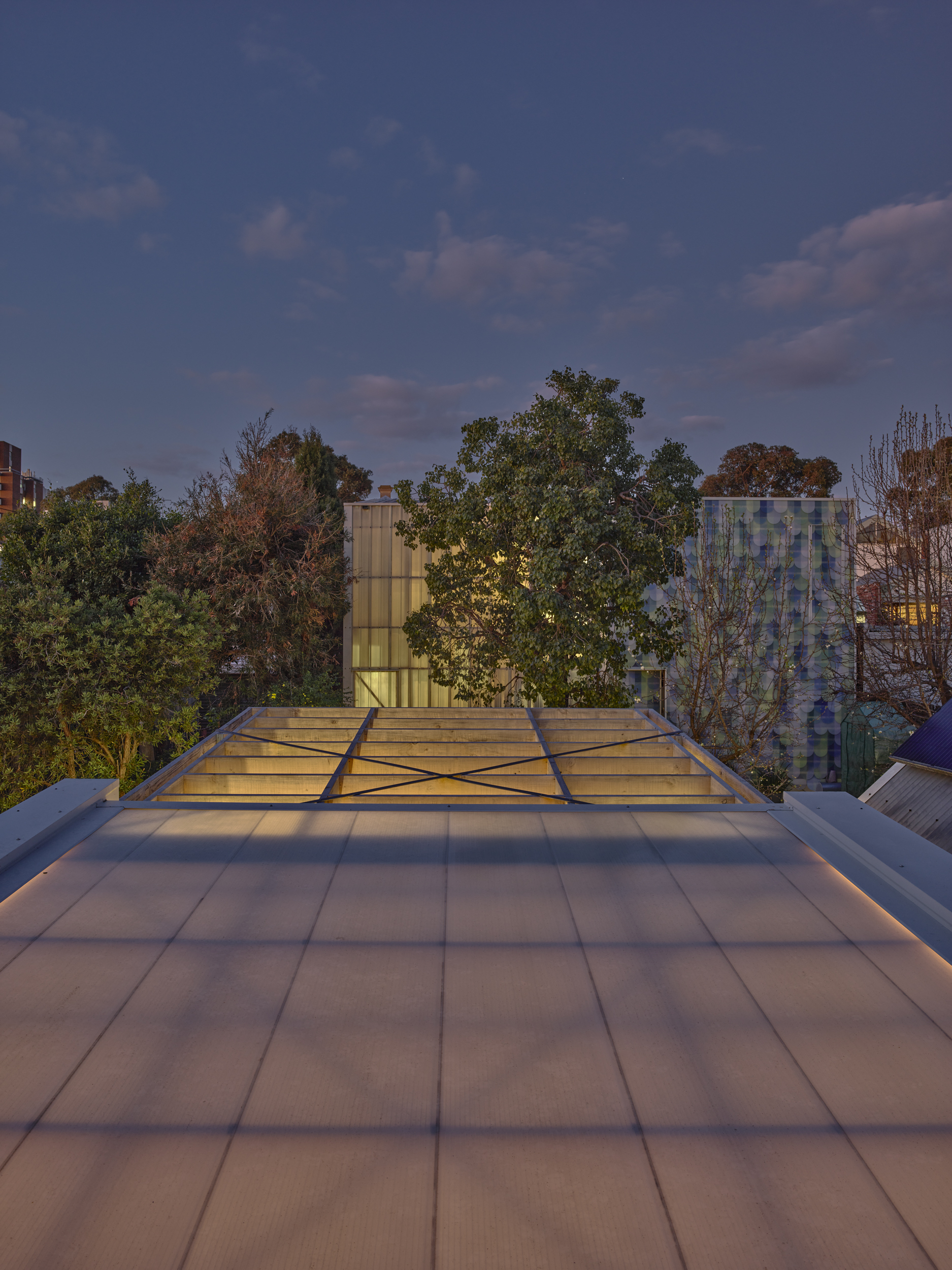 Rooftop terrace with tiled paving and glass skylight panels overlooking neighboring treetops at twilight