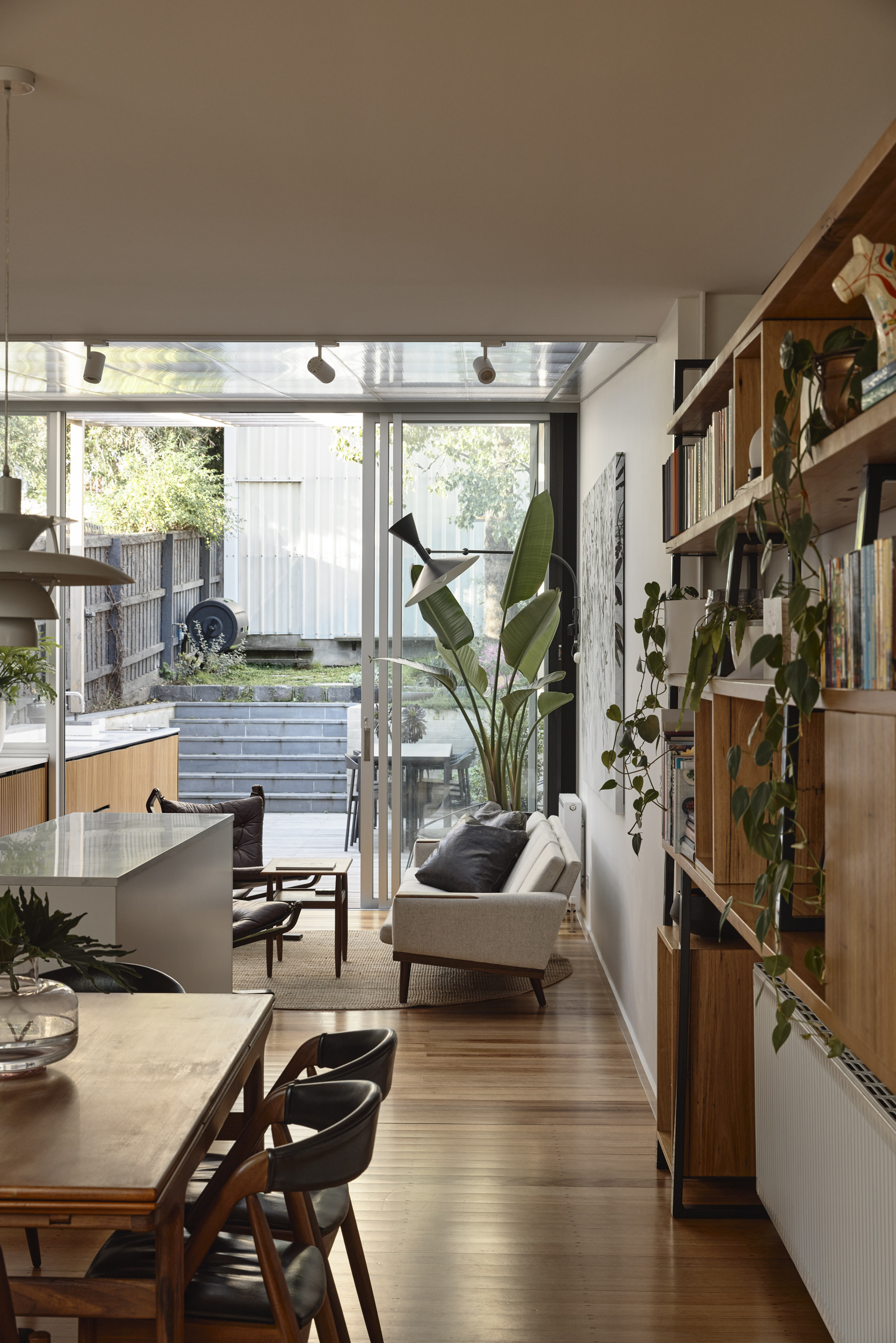 Corridor with timber shelving wall and glazed doors opening to sunlit courtyard and tree