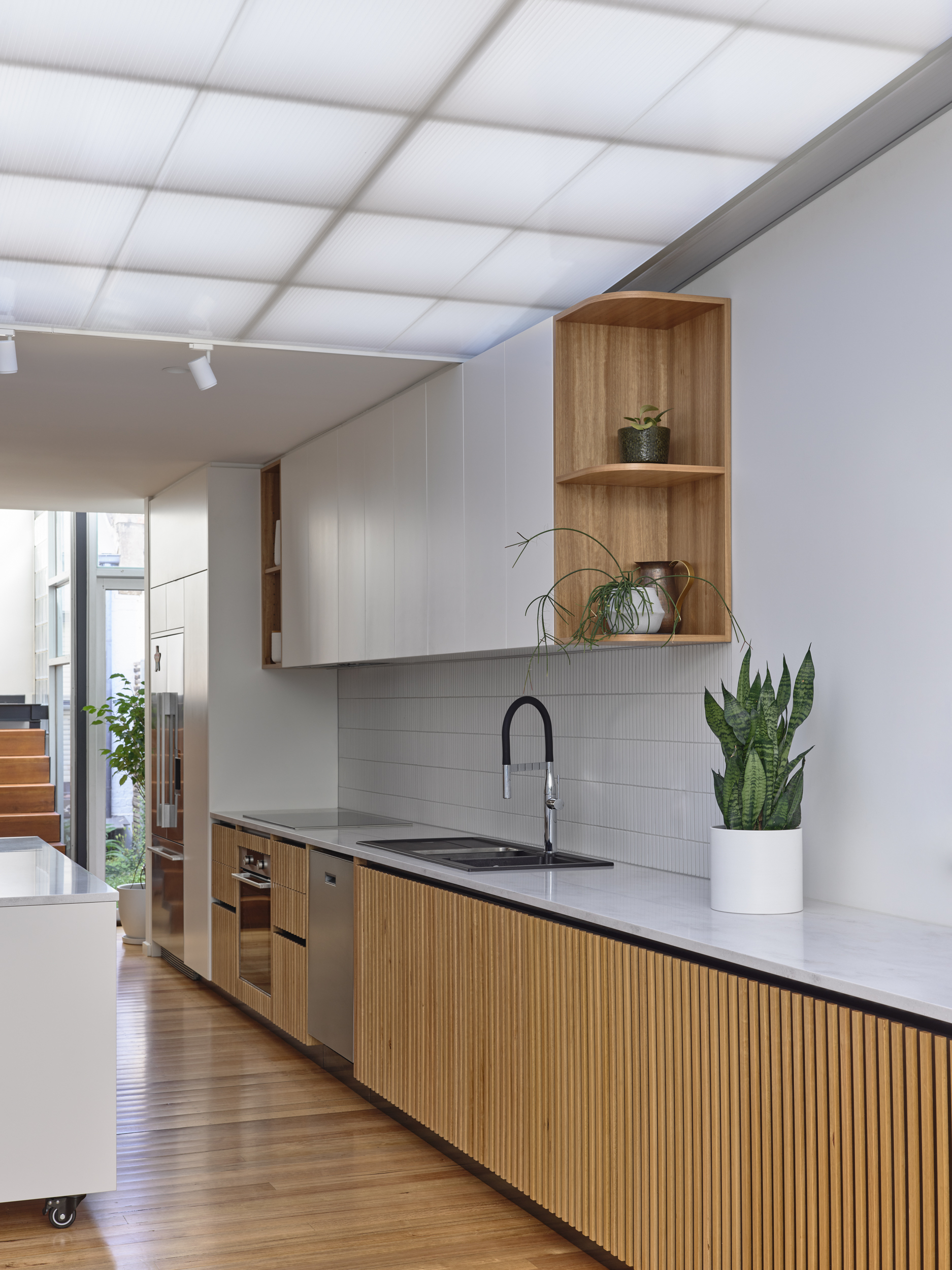 Galley kitchen featuring timber-slat cabinetry and open timber shelving with potted plants