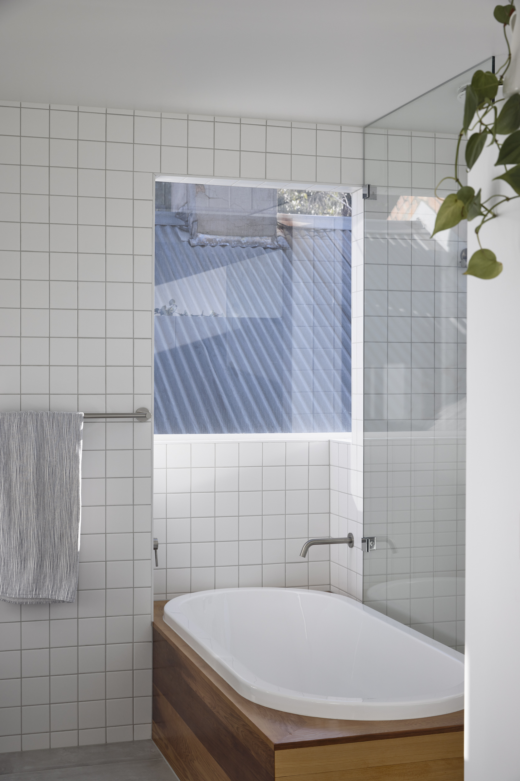Bathroom with white square-tile walls, timber-clad tub surround, and frosted glass shower screen