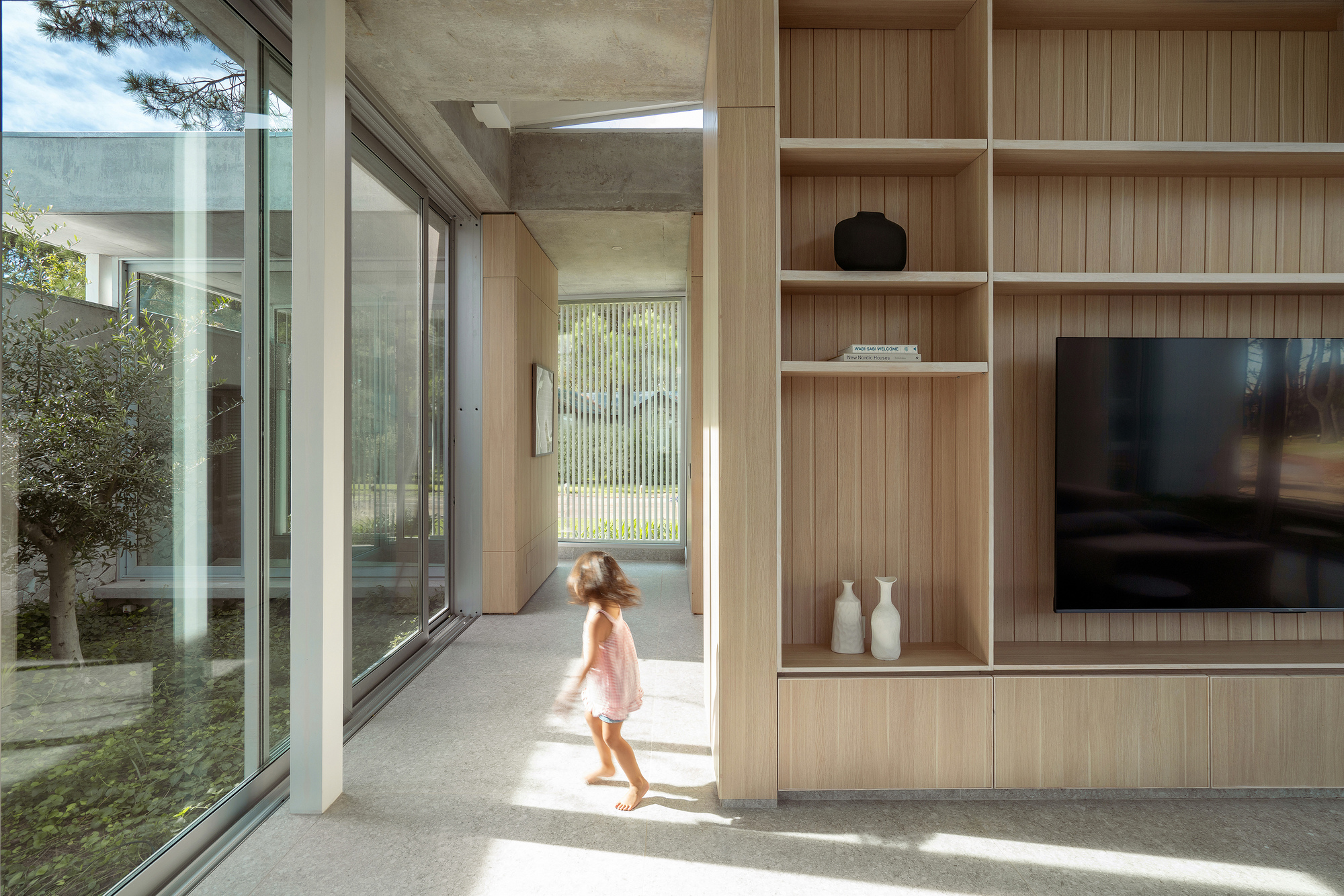 Interior corridor with timber shelving and a child running through sunlit space toward a courtyard