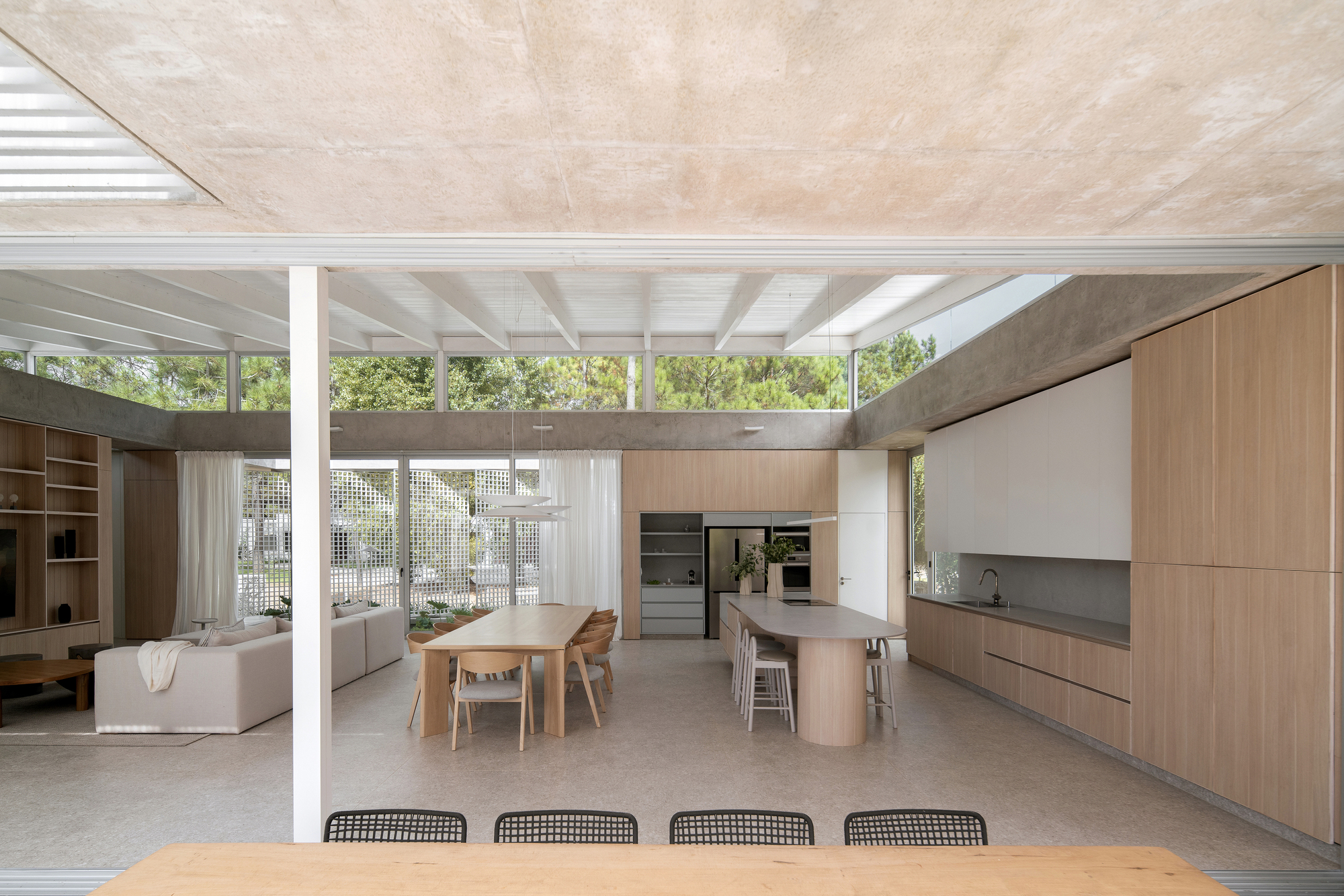 Open-plan interior with timber kitchen, dining table and slatted white ceiling under natural daylight