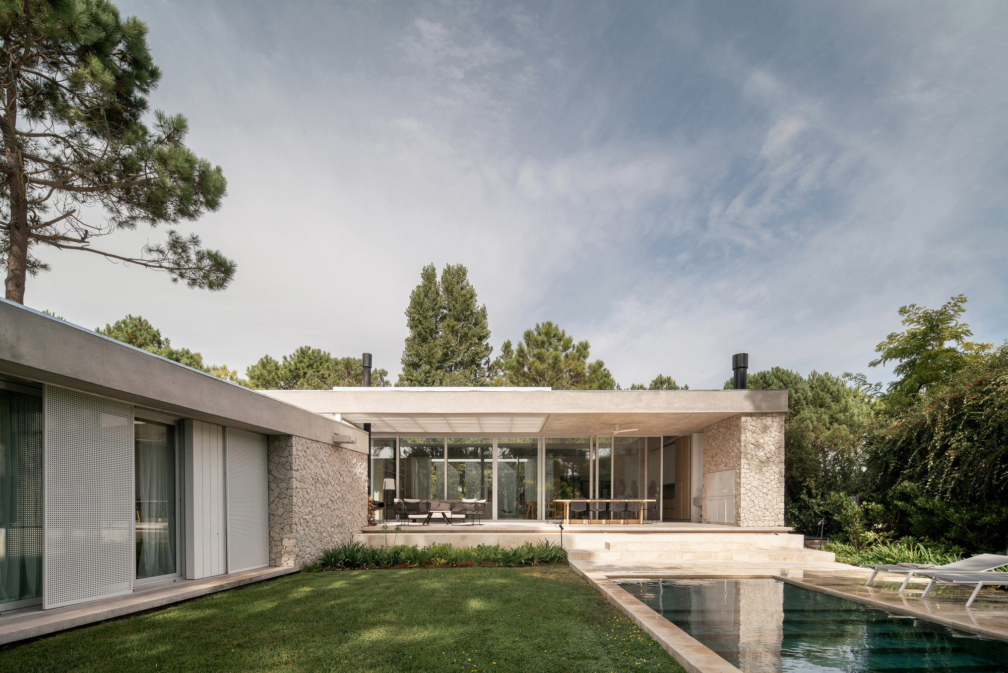 Garden view showing the raised pavilion with slatted roof and stone walls beside the pool
