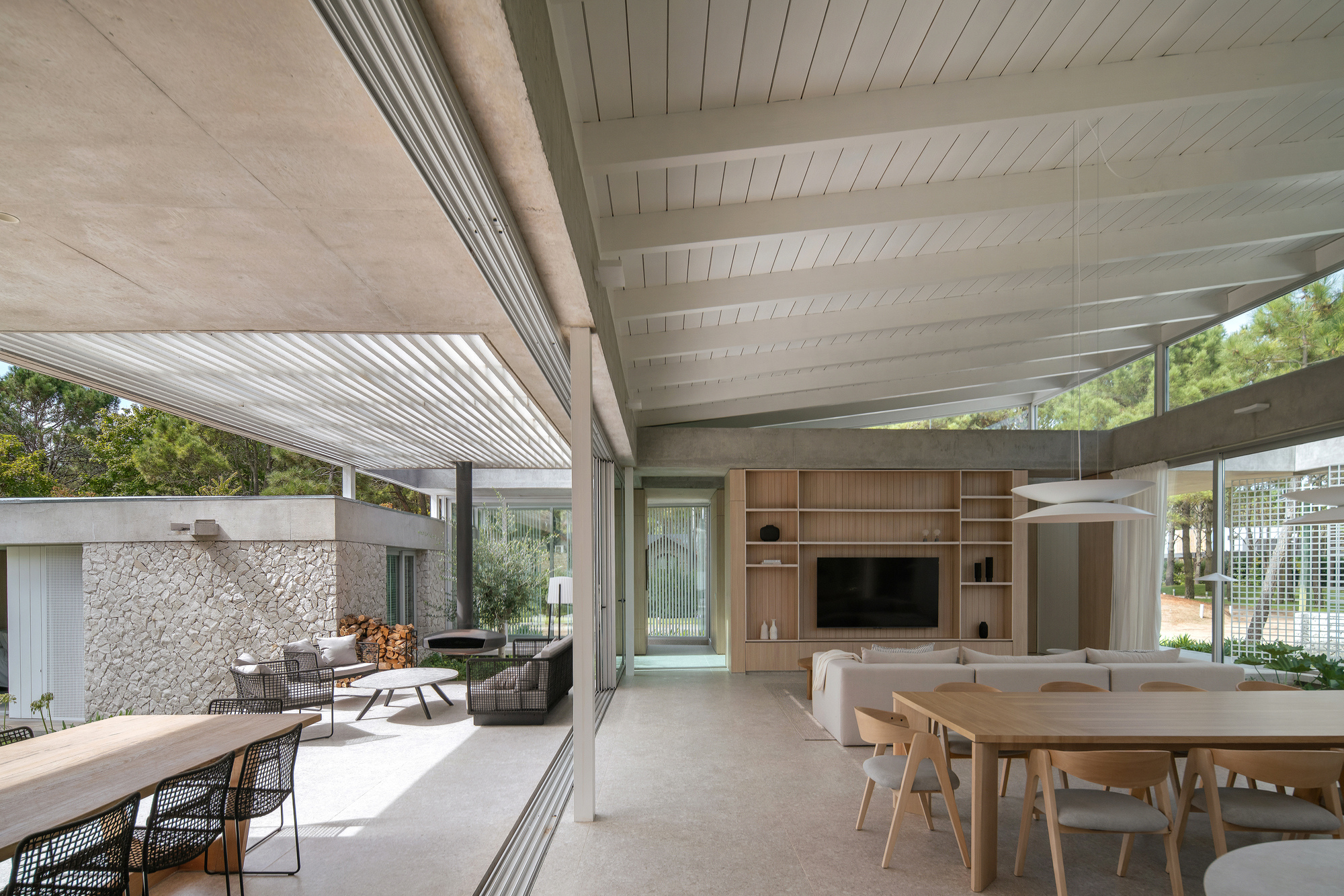 Living and dining area with exposed concrete beams and floor-to-ceiling glass opening to covered terrace