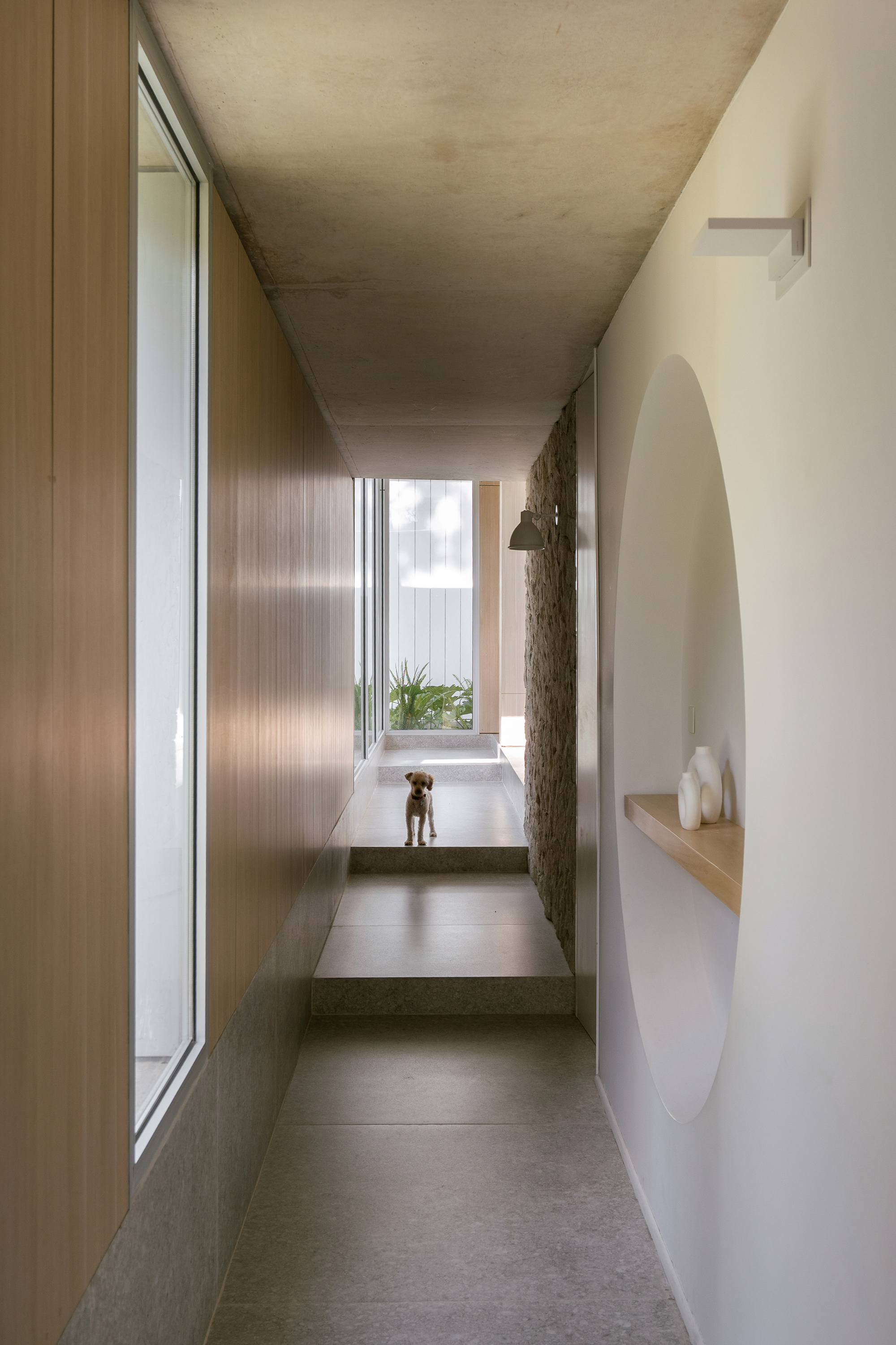 Narrow corridor with concrete ceiling, timber wall panels and arched niche with floating timber shelf