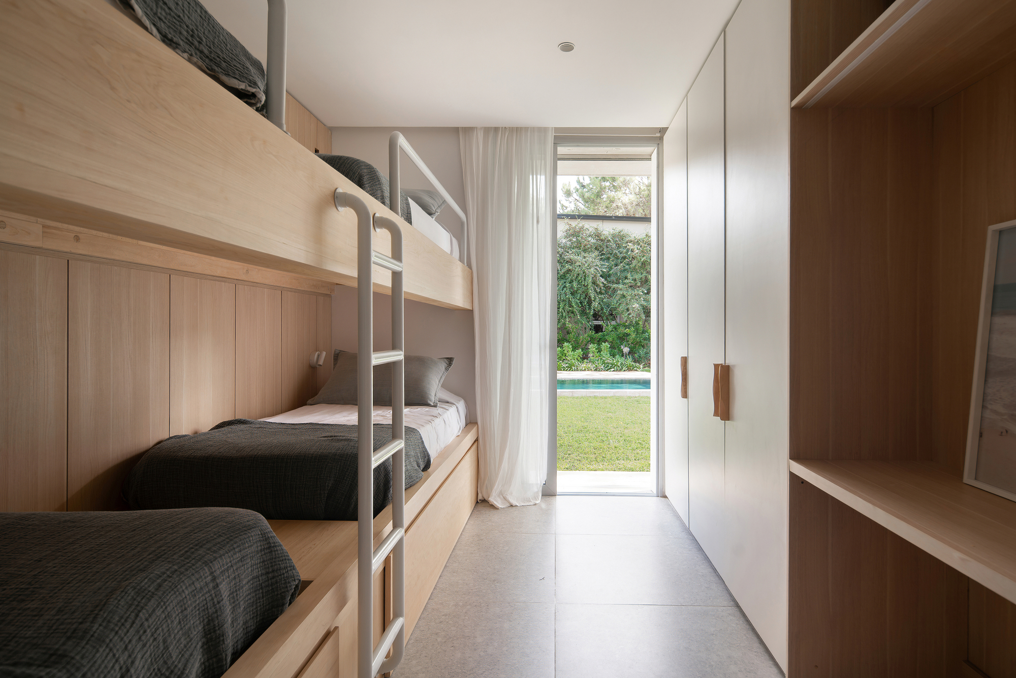 Bunk bed room with timber cabinetry opening to garden through sheer curtains and glass door