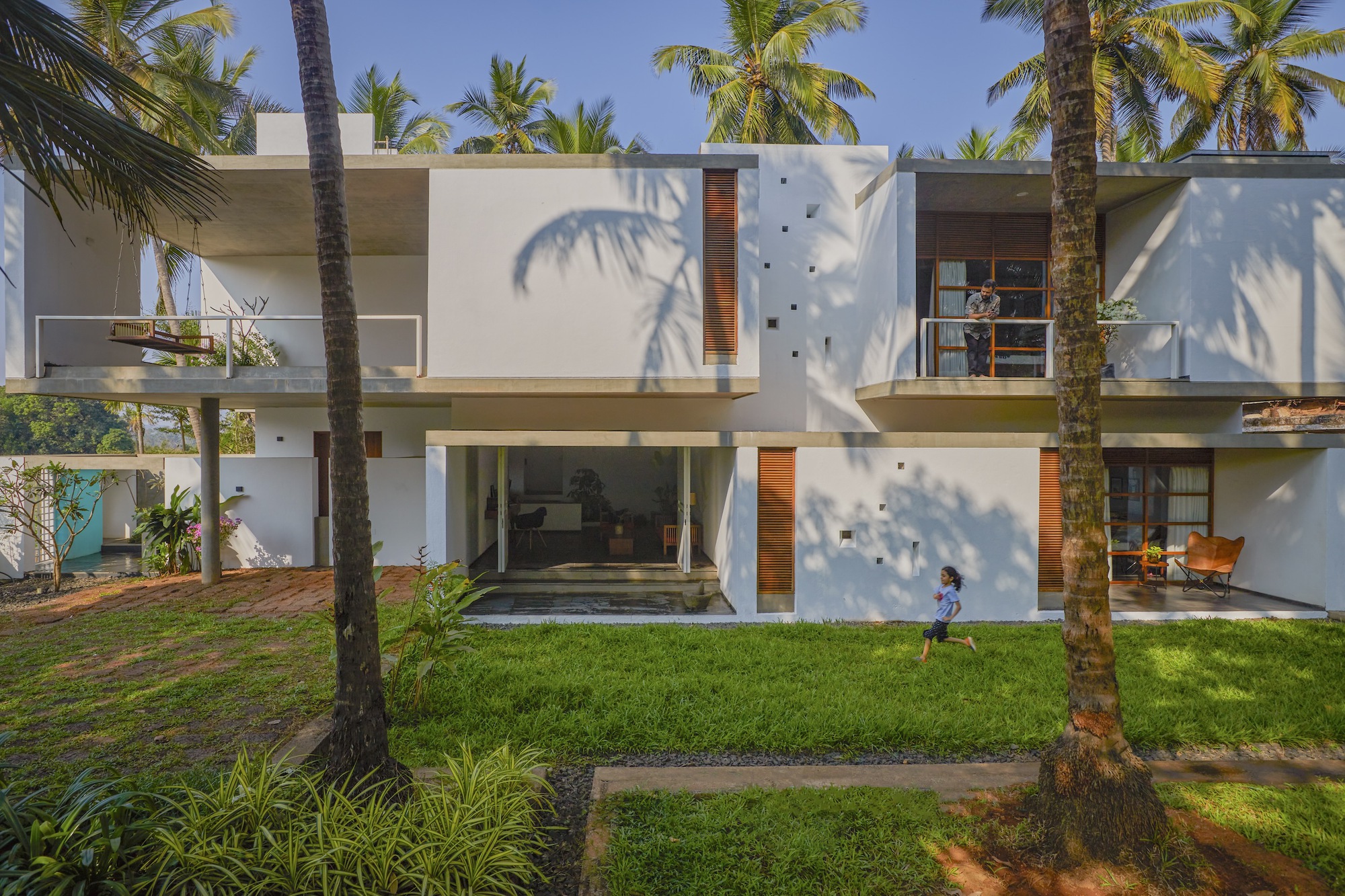 Garden facade with white rendered walls and timber shutters casting palm shadows in afternoon light