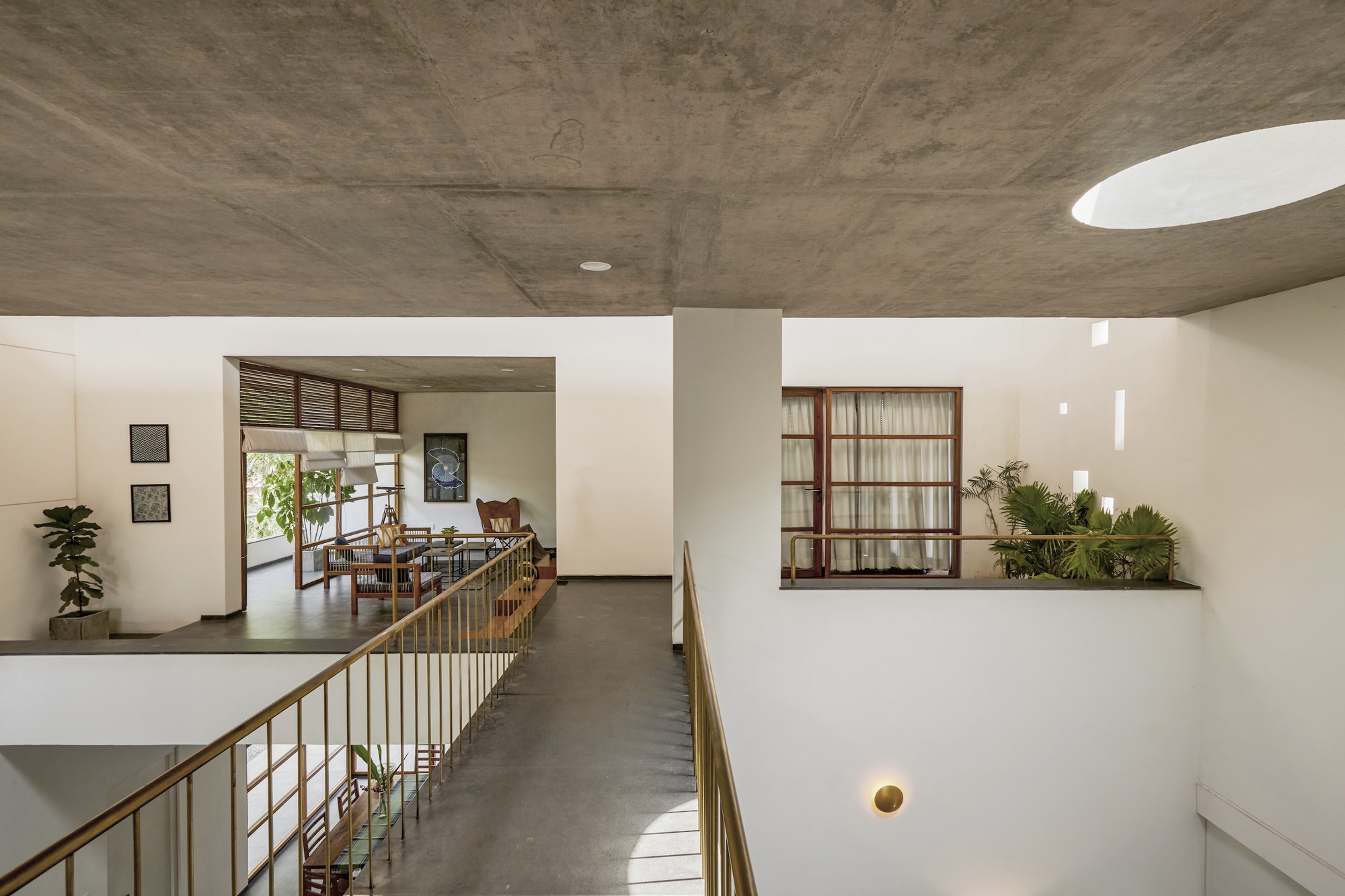 Upper-level corridor with exposed concrete ceiling, brass railings and potted plants in a window niche