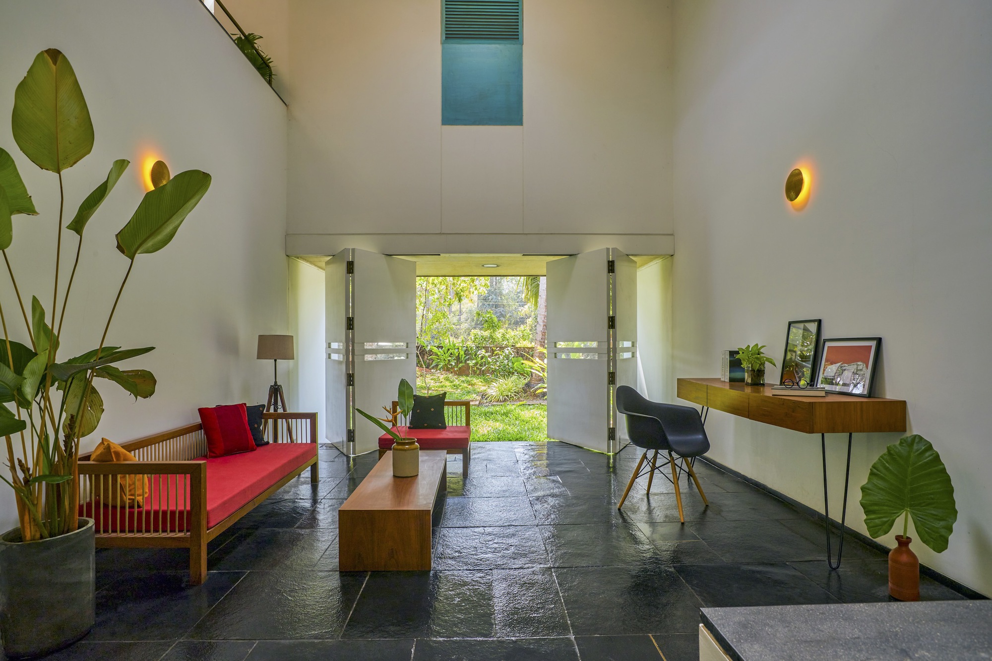 Double-height entry hall with black stone flooring and circular wall sconces flanking a garden view