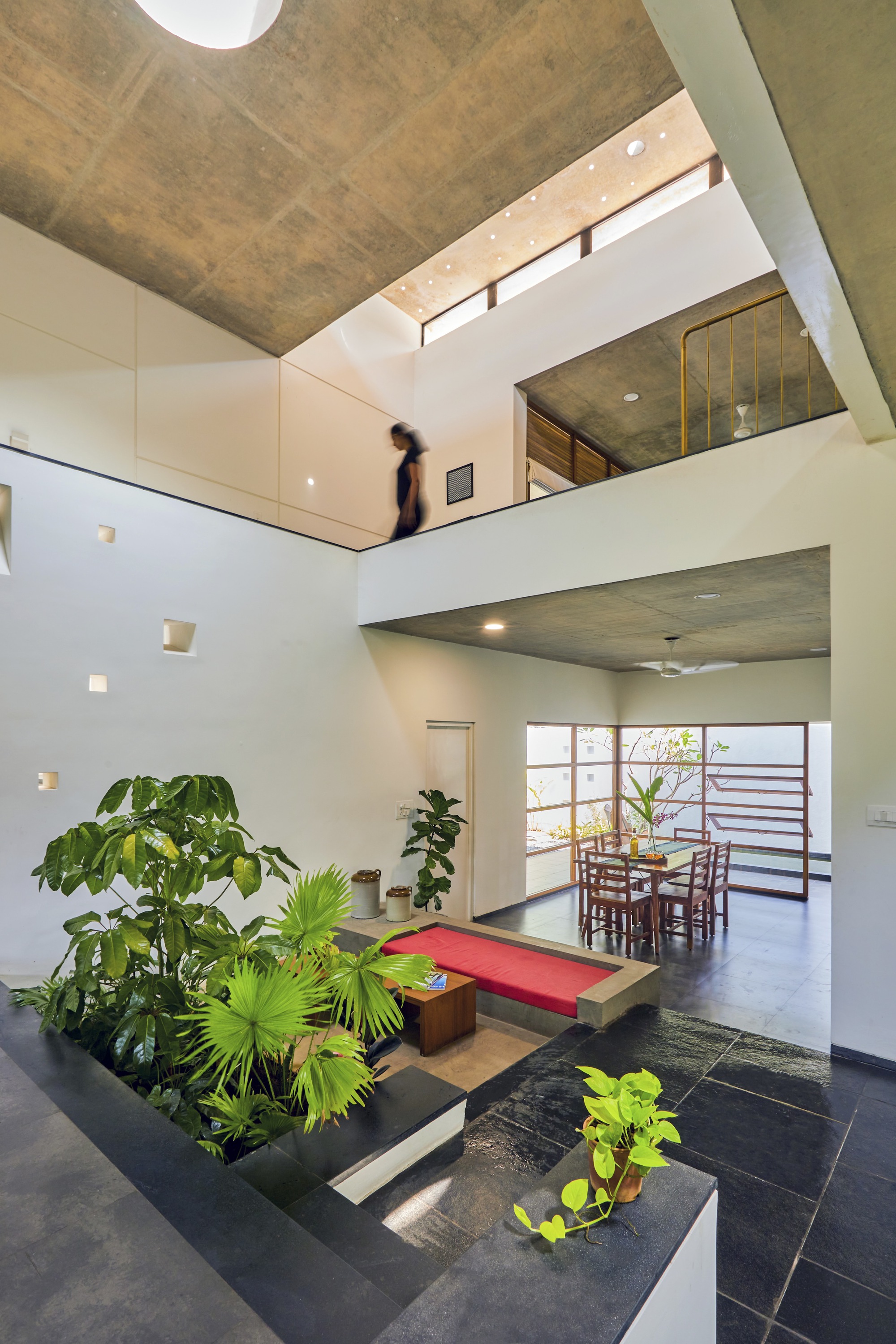 Interior courtyard with planted beds and red bench beneath a skylit void and mezzanine balconies