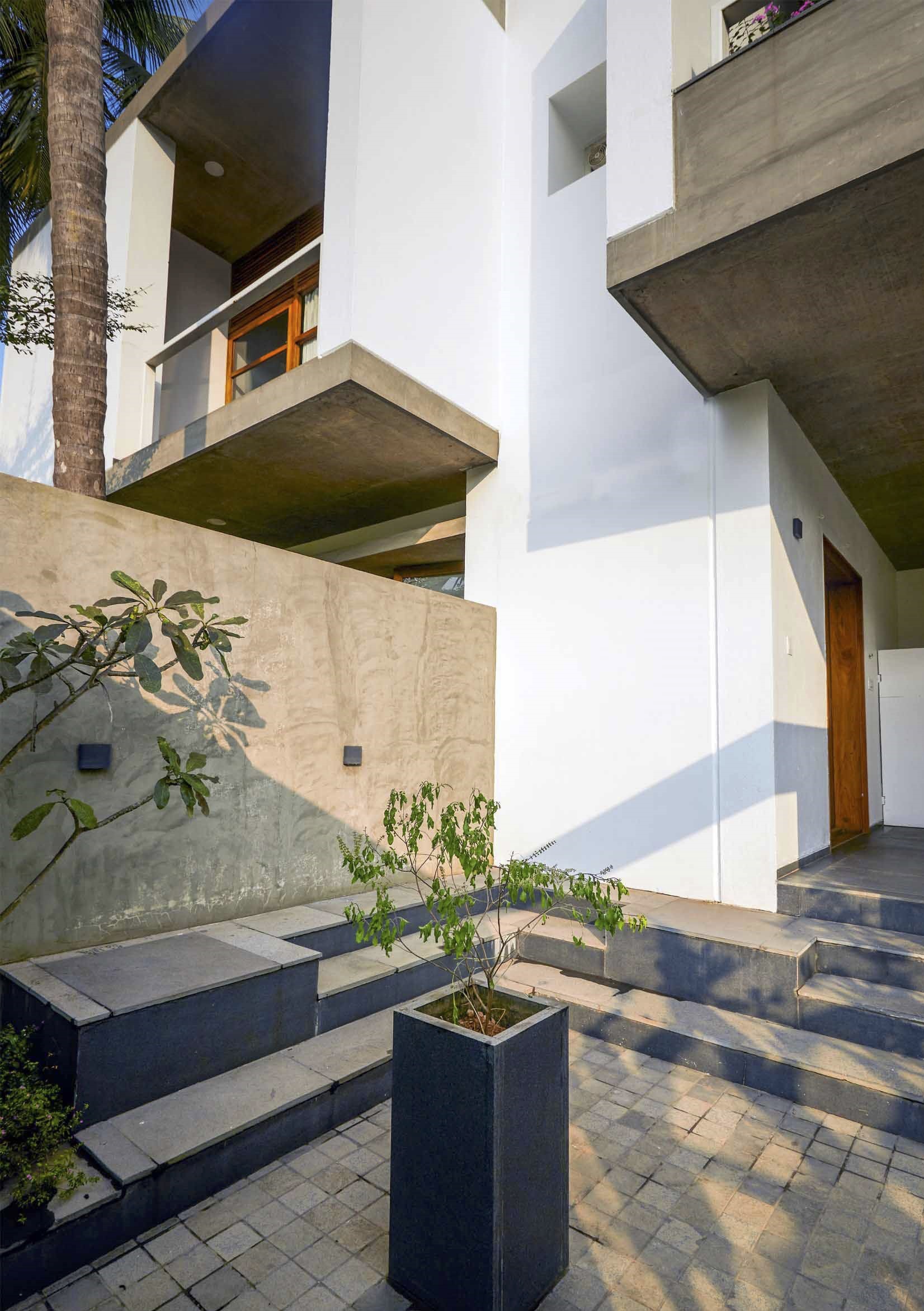 Entry courtyard with cantilevered concrete balconies, stone steps, and planters beneath a palm tree