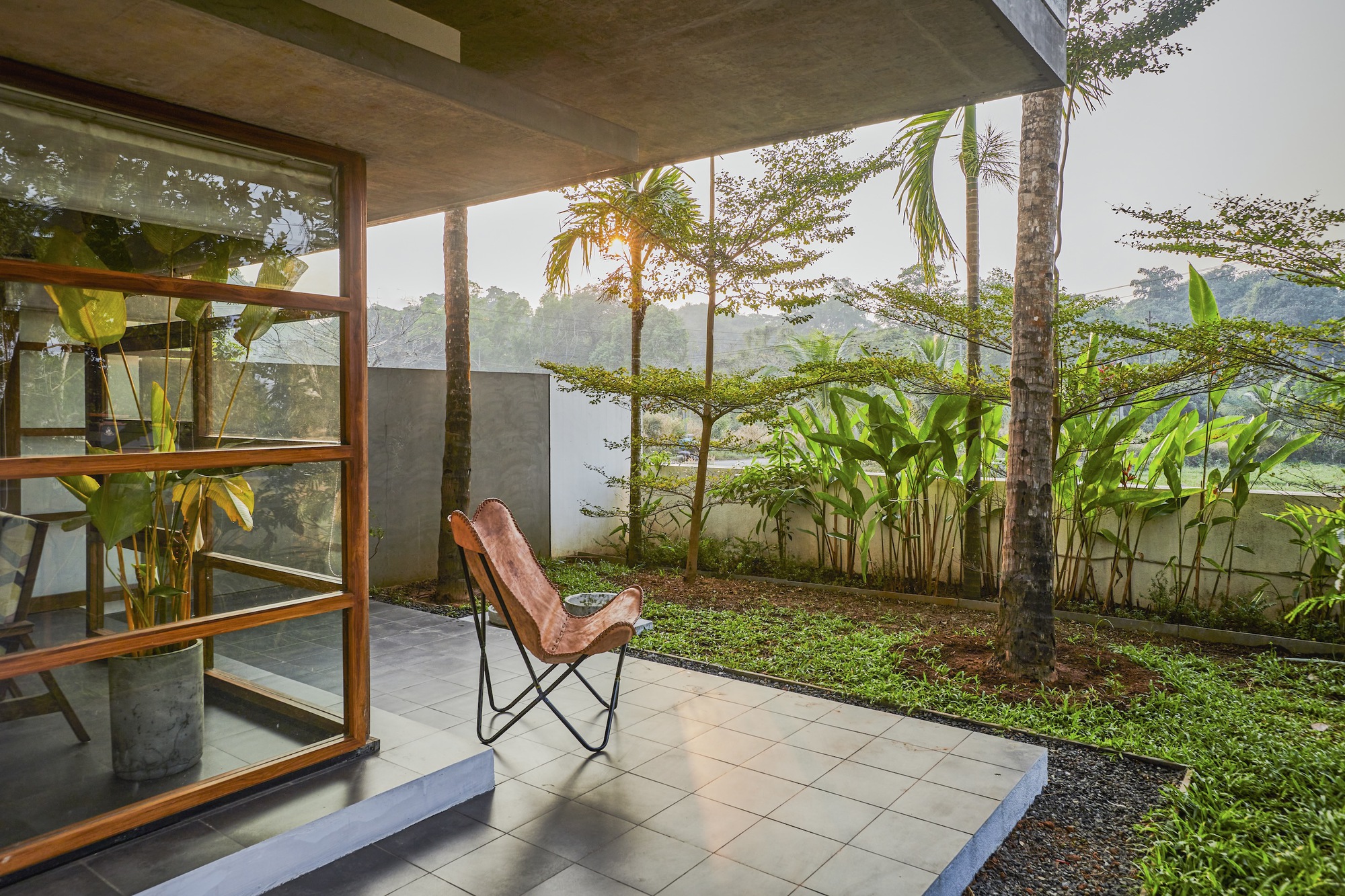 Private terrace with leather chair opening to planted garden through timber-framed glass doors at dawn