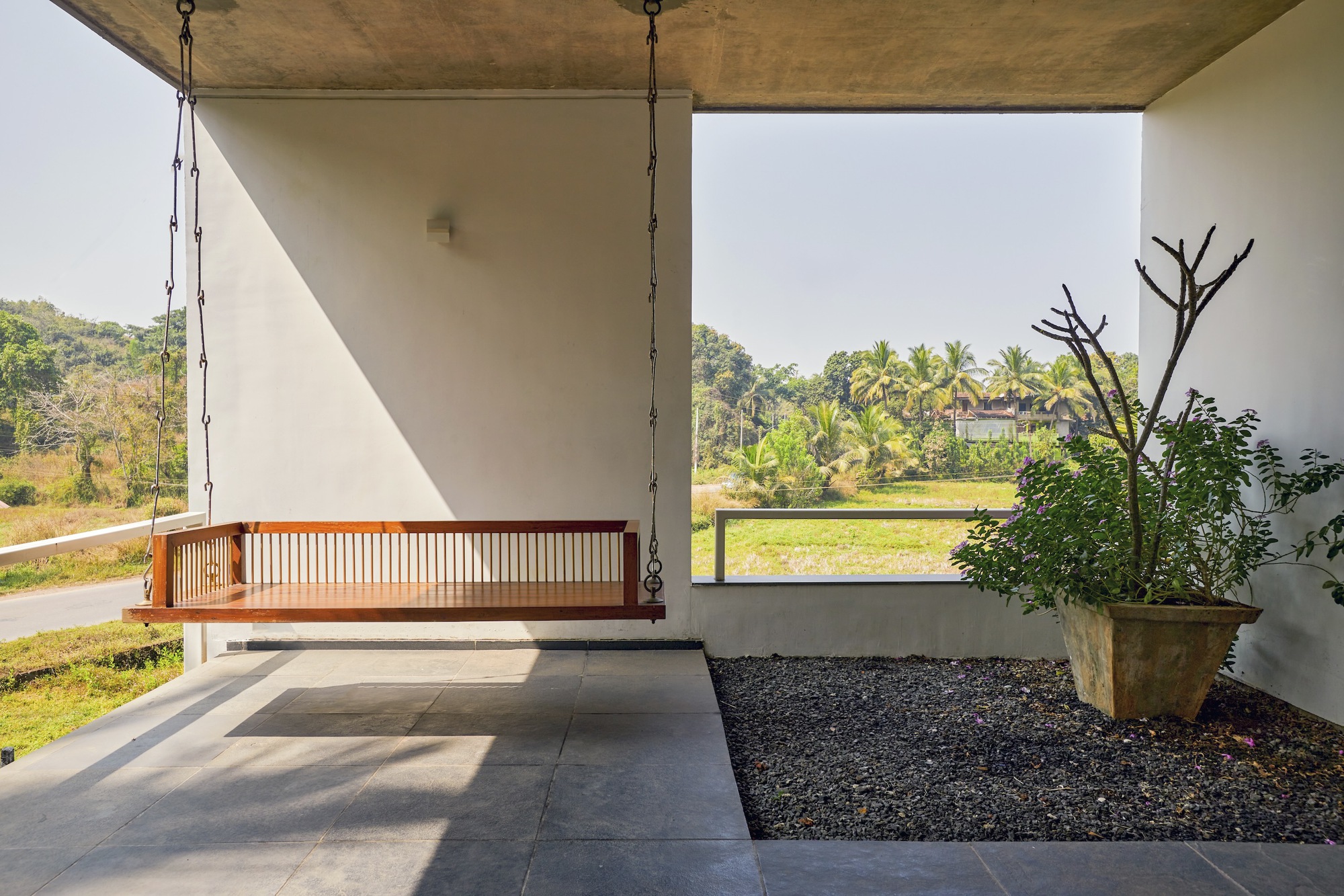 Covered porch with suspended timber daybed overlooking planted beds and distant palms