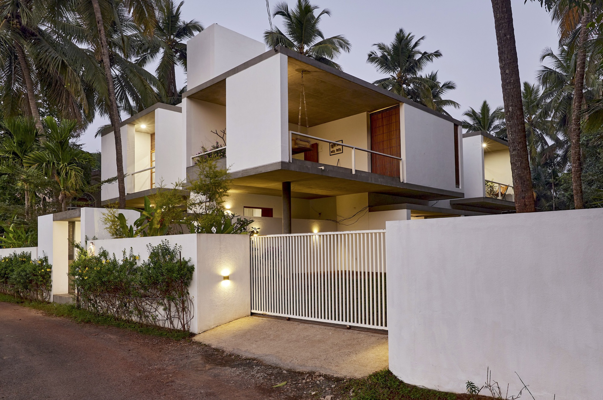 Street facade at dusk showing stacked white volumes with timber screen gate and uplighting