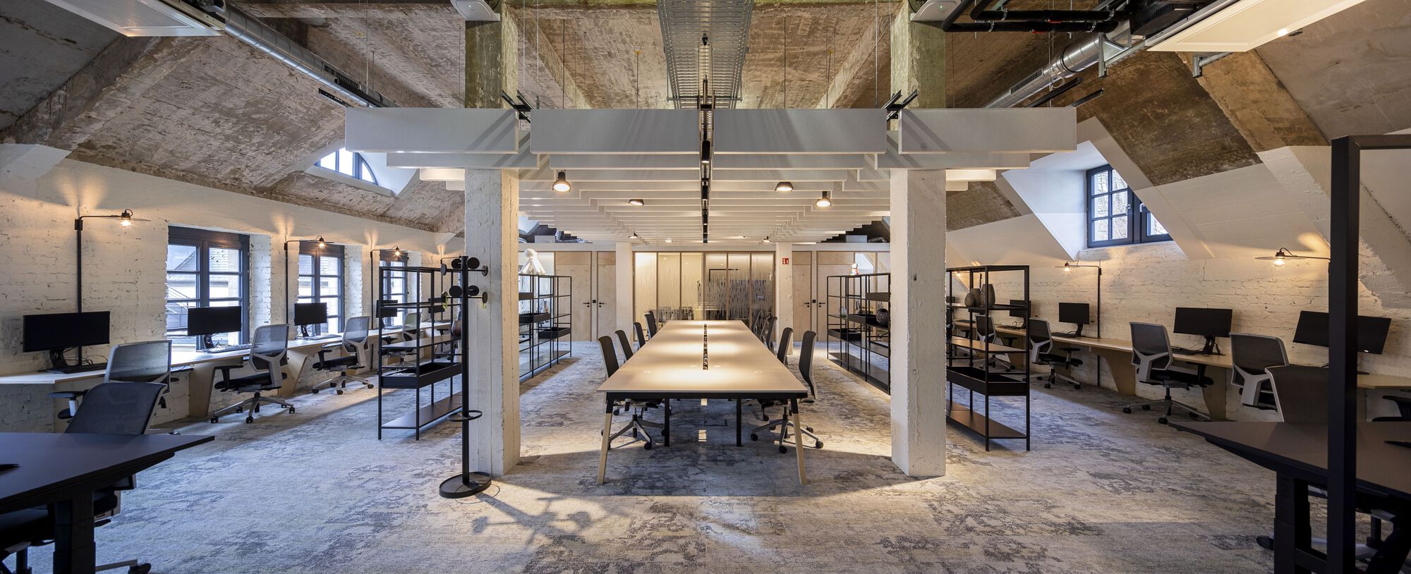 Central conference table surrounded by glass-walled meeting rooms beneath angled concrete vault ceilings