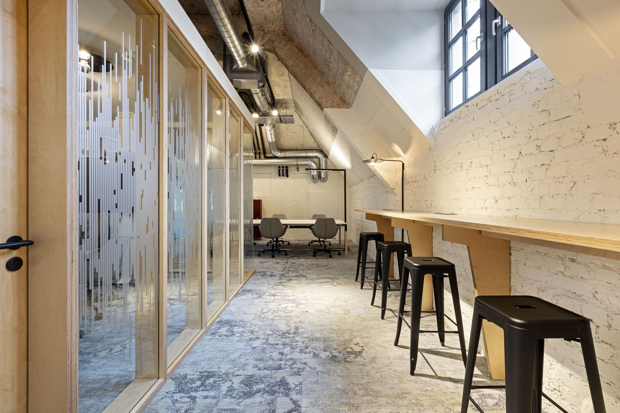 Corridor with timber counter and bar stools against whitewashed brick wall beneath sloped concrete ceiling
