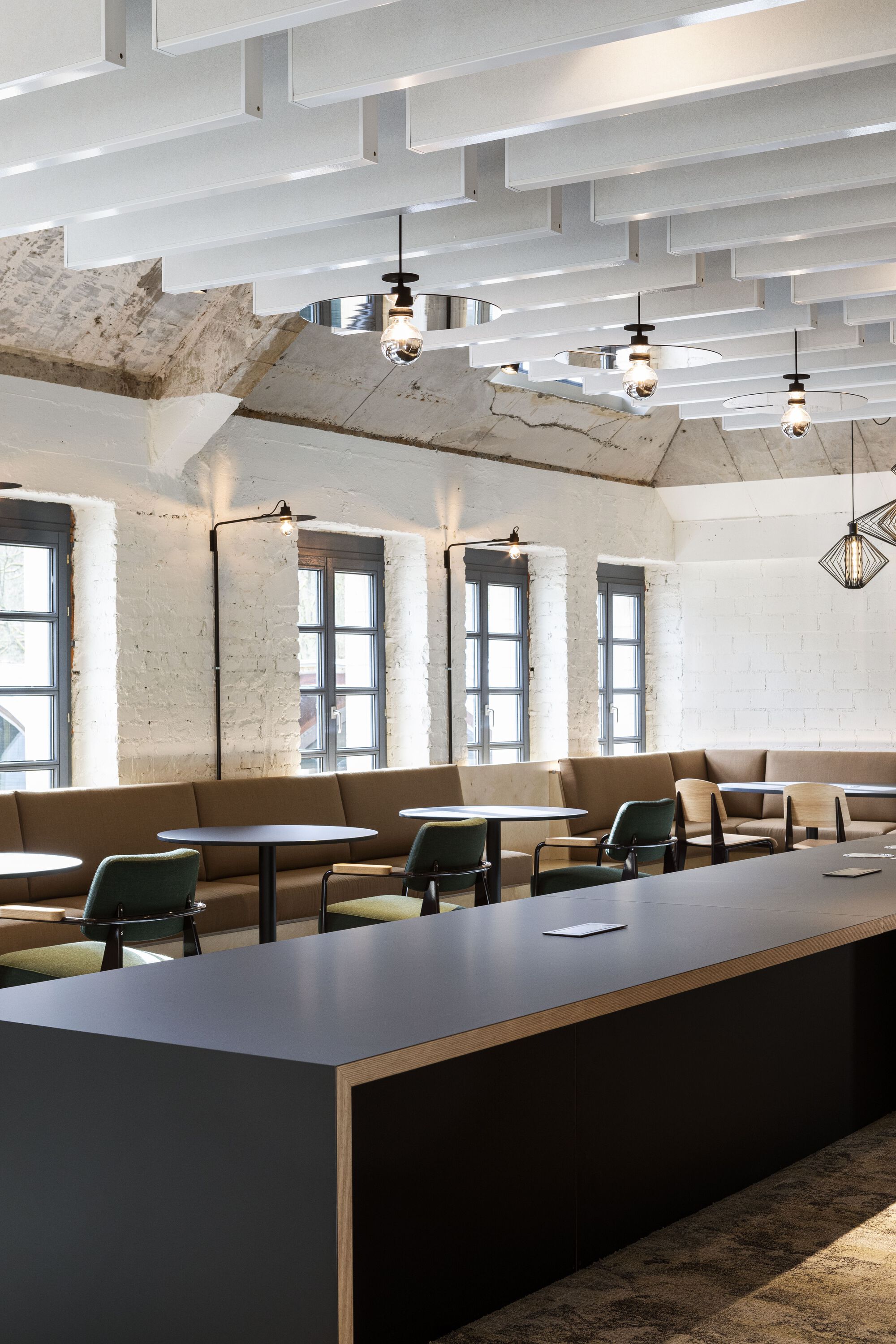 Cafe seating area with tan upholstered banquettes beneath white acoustic baffles and exposed concrete vaults